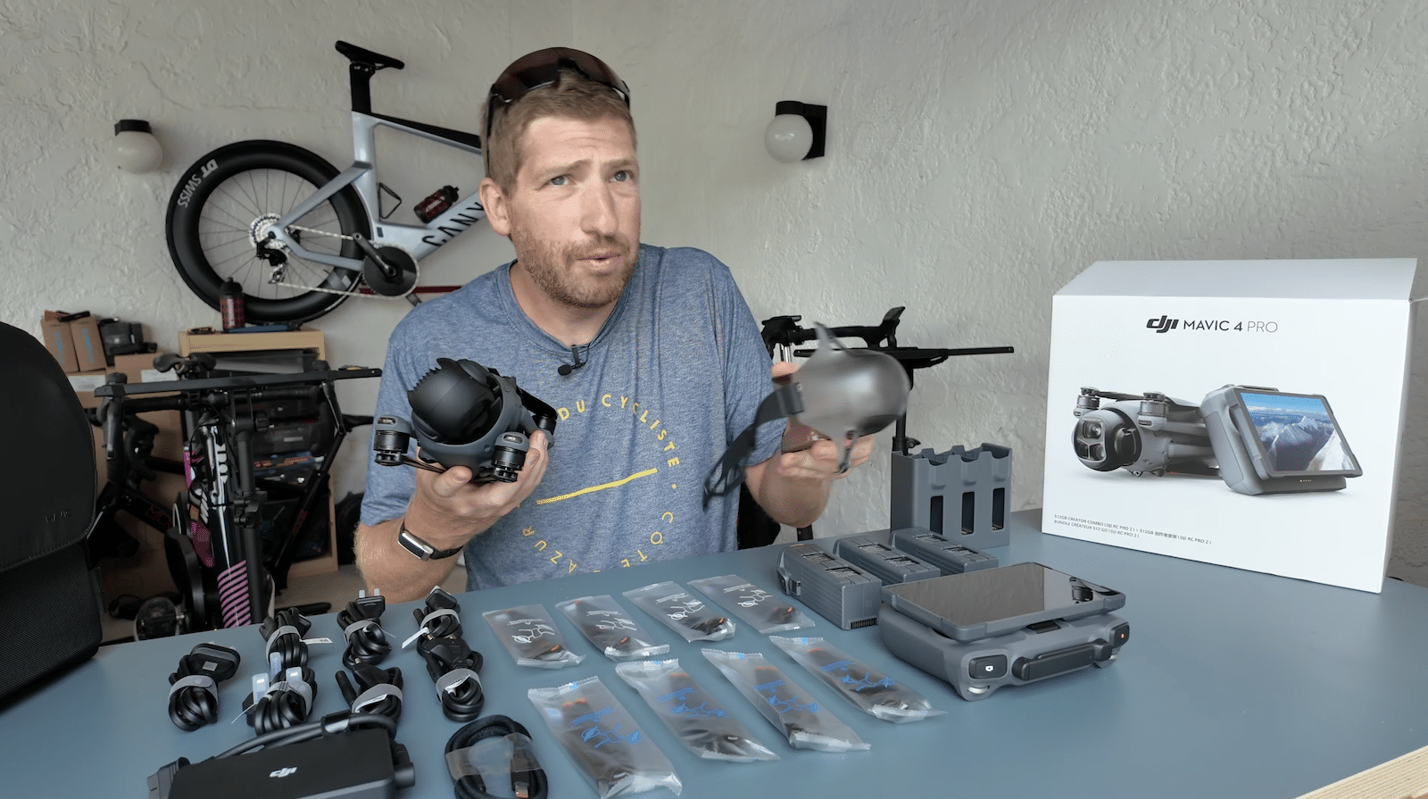 A reviewer holds drone parts at a bench spread with the combo box and accessories.