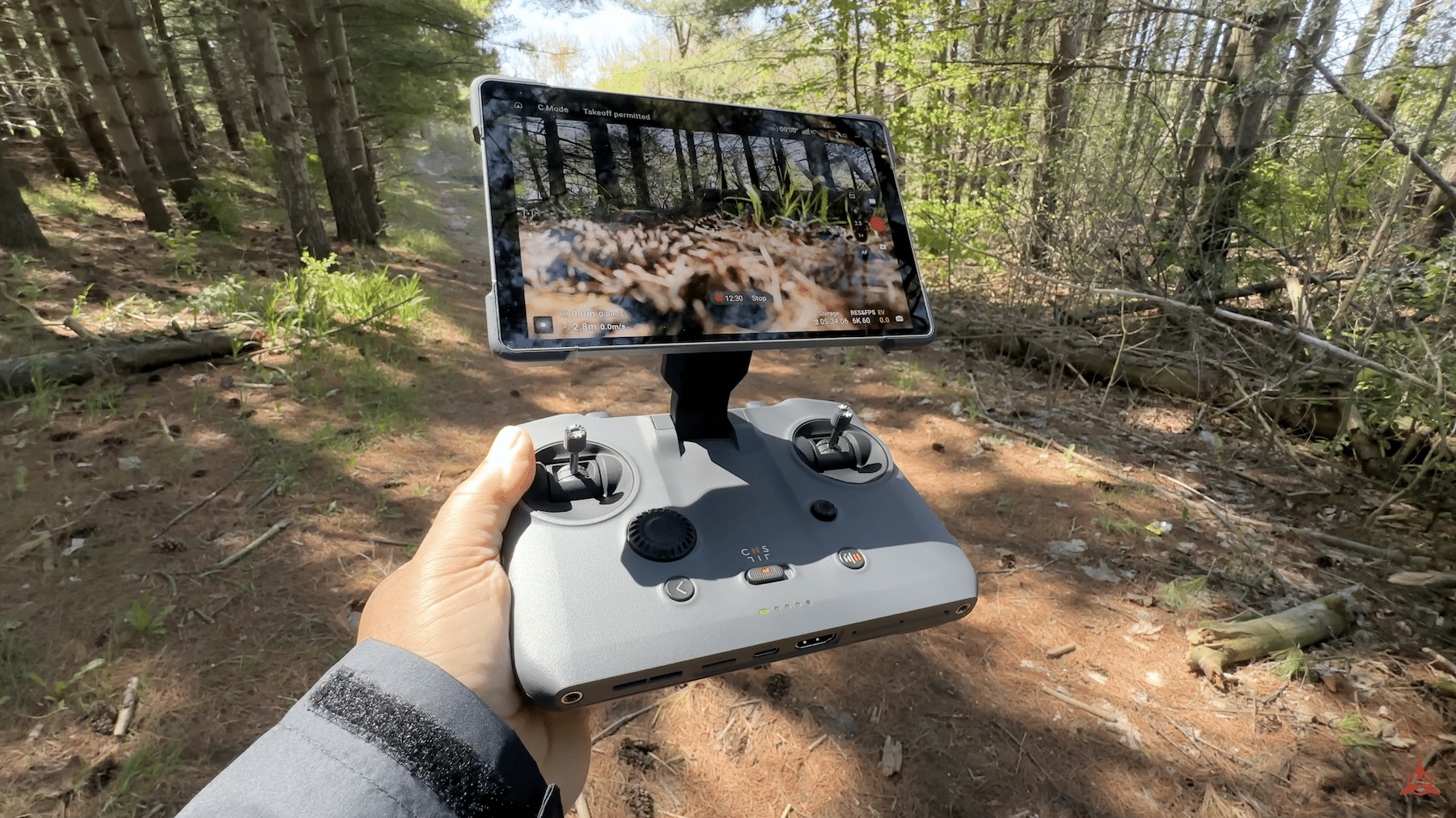 Hand holds a DJI RC Pro 2 controller playing footage on a forest trail.