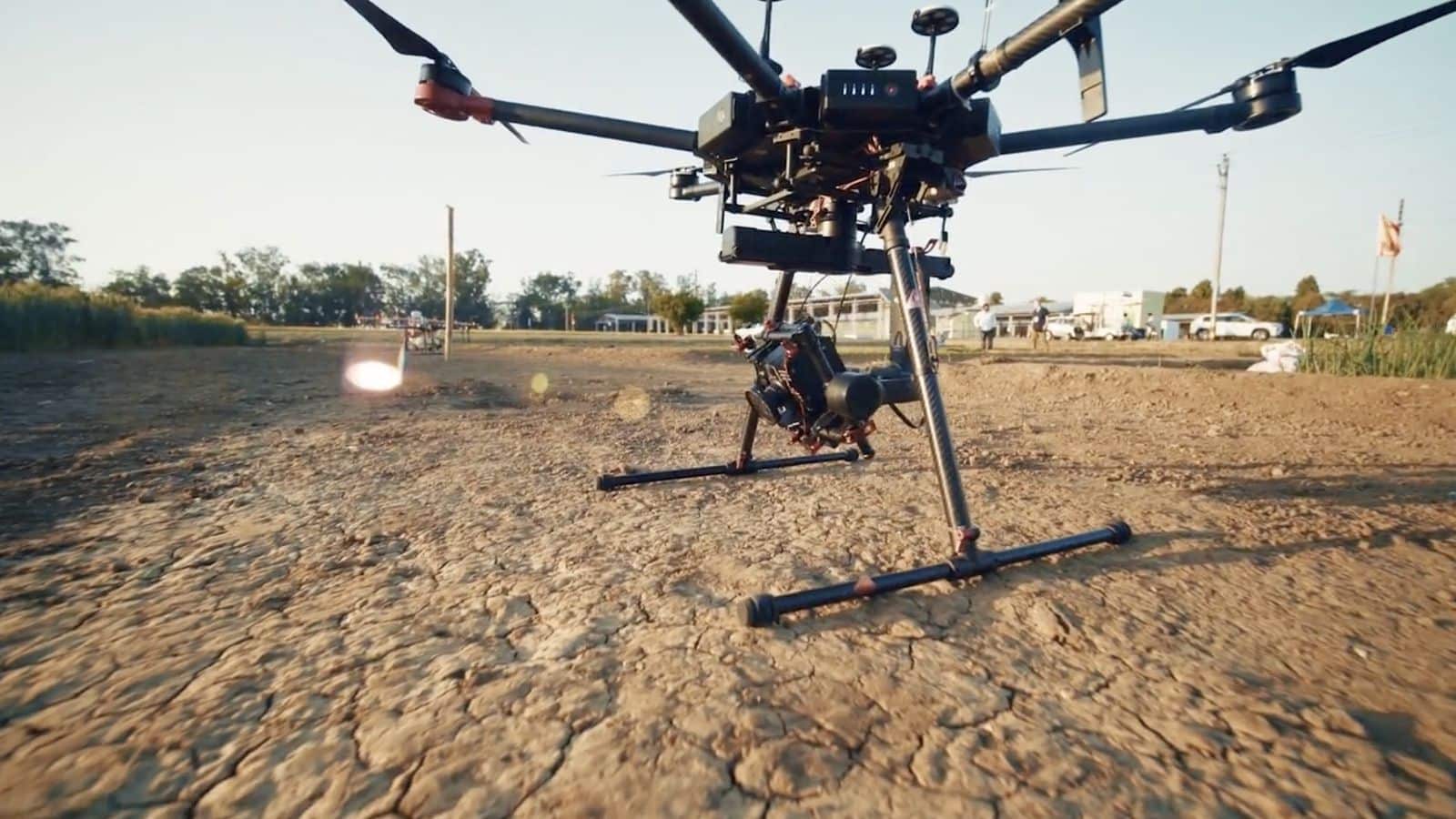 Low-angle view of an agricultural spray drone parked on cracked dry earth.