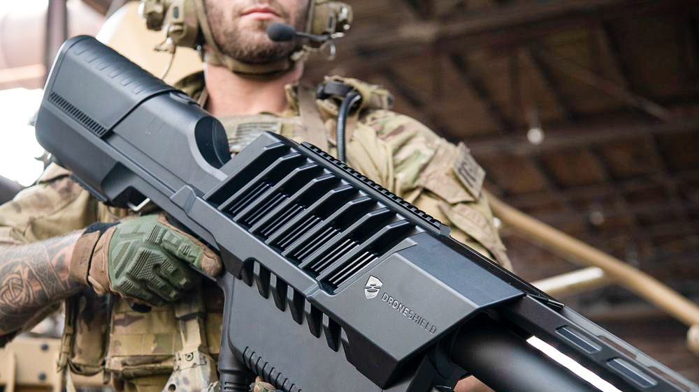 A soldier shoulders a large counter-drone jamming gun in a shaded room.