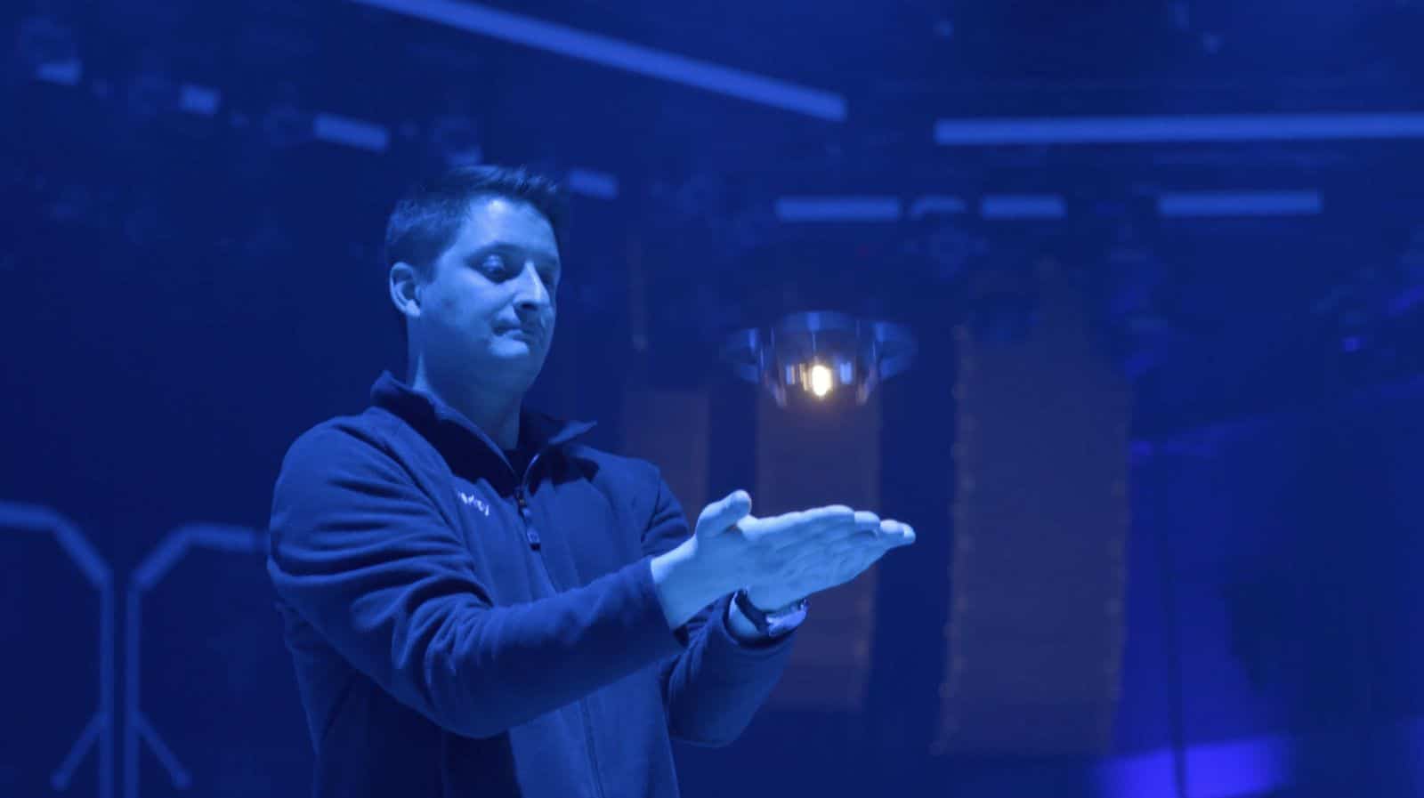 Presenter in a blue-lit hall catching a single micro drone in his cupped hands.