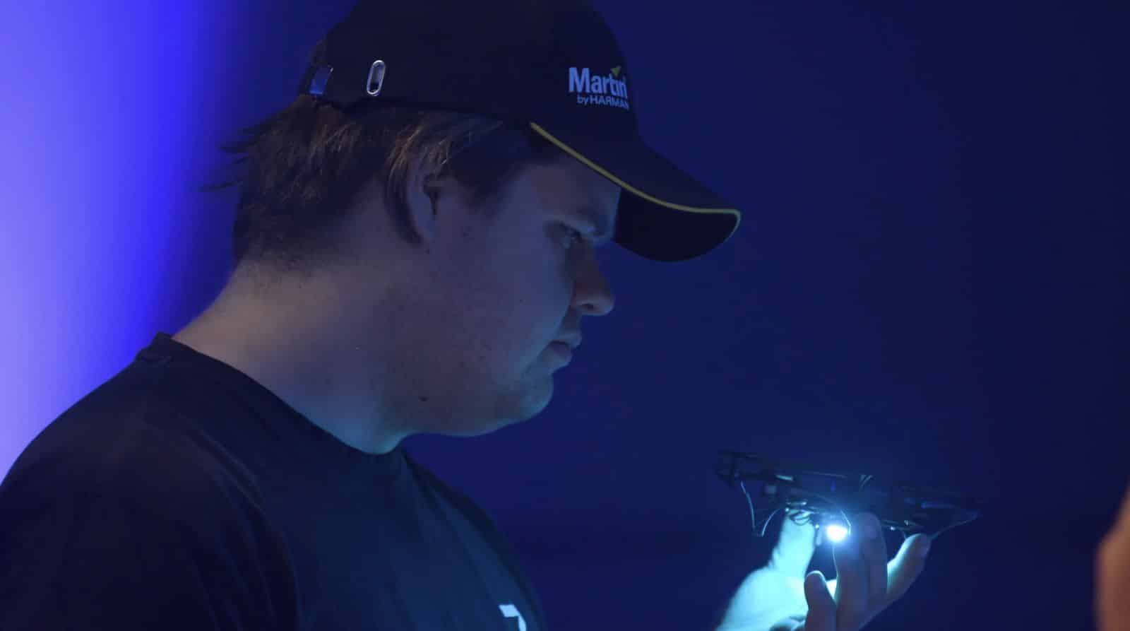 Crew member in a Martin Professional cap holding a lit micro drone in blue light.