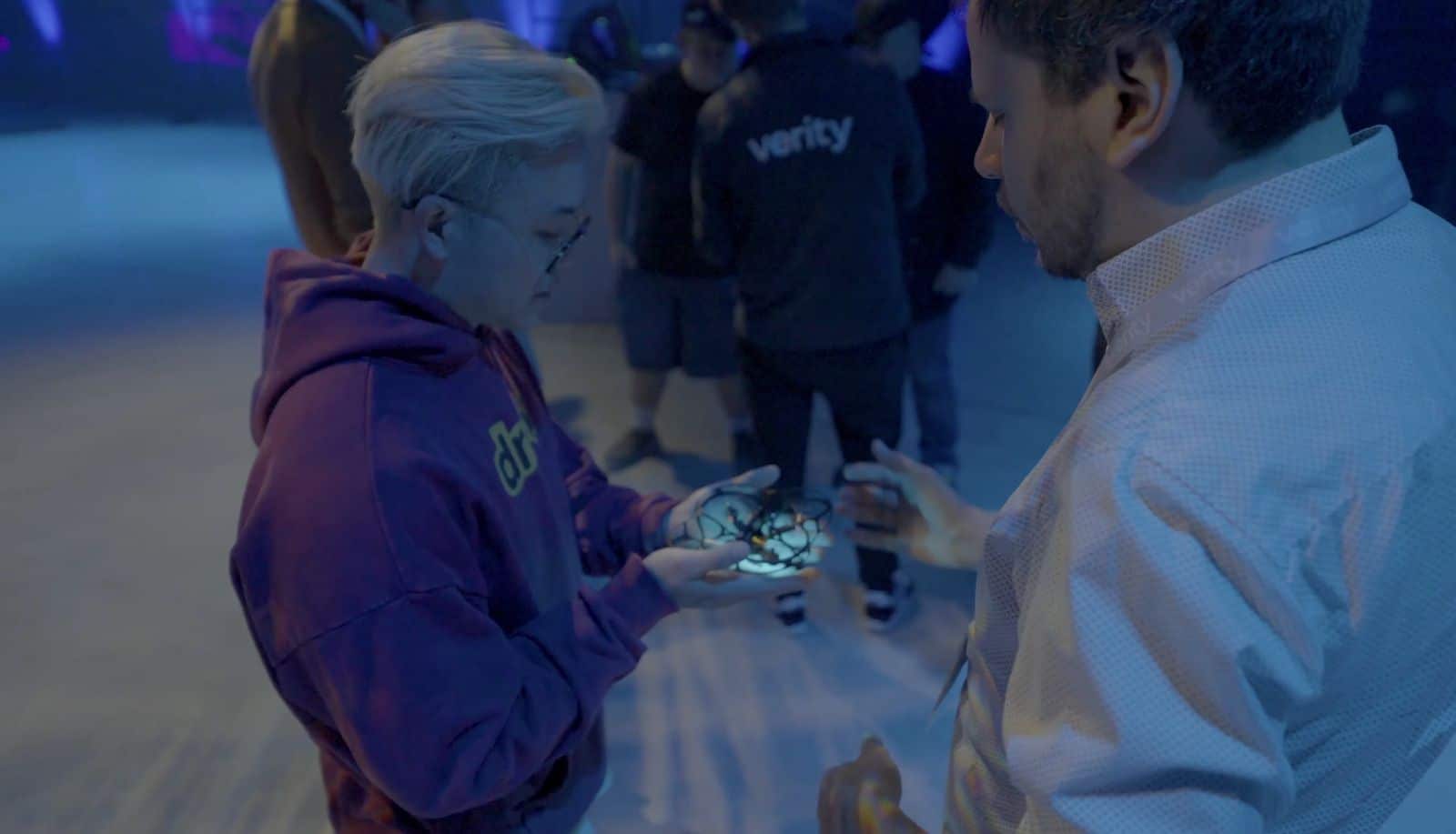 Attendees leaning in to inspect a micro drone held in an open palm.