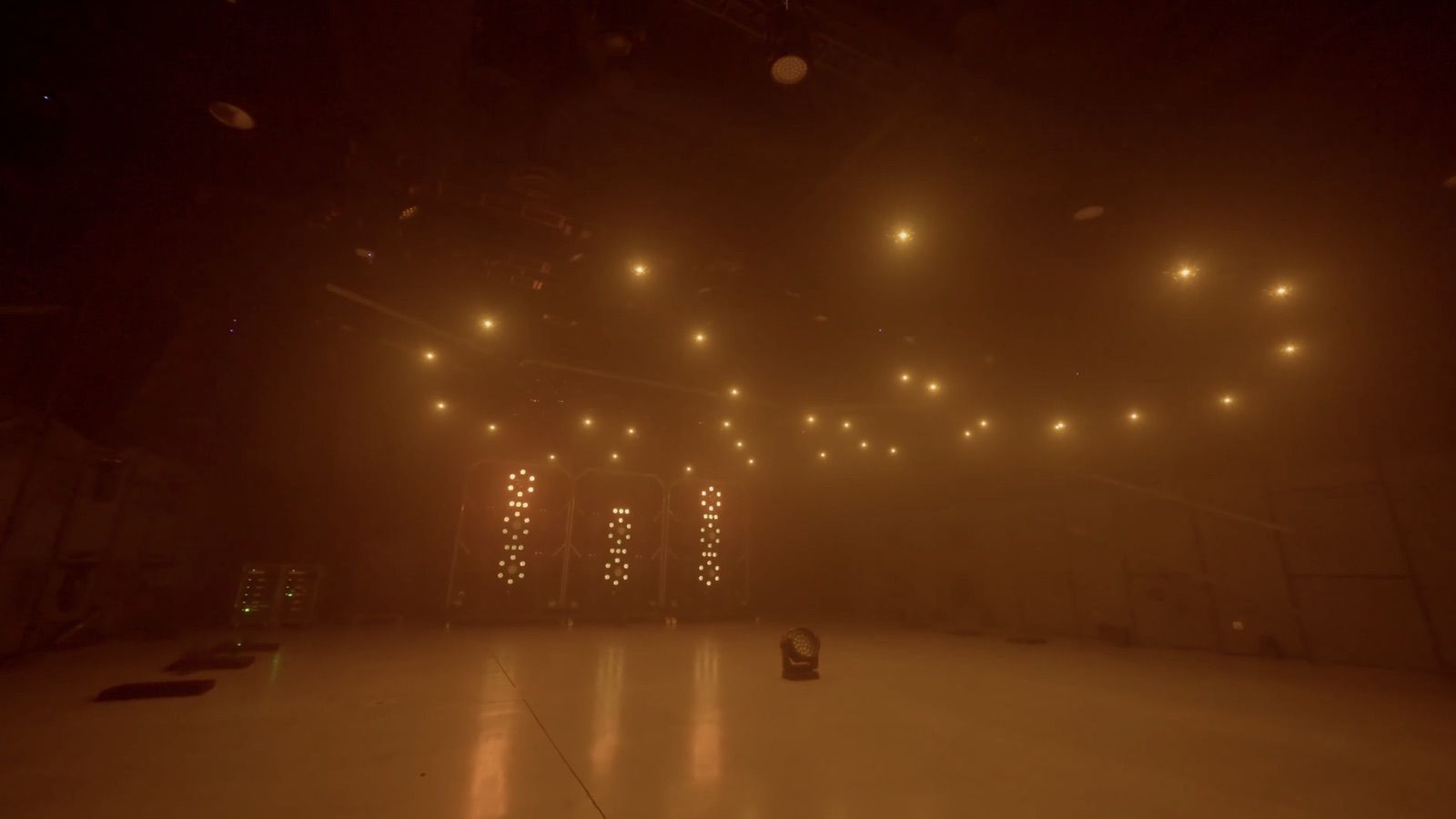 Amber drone formation arcs across a smoke-filled stage above the lighting rig.