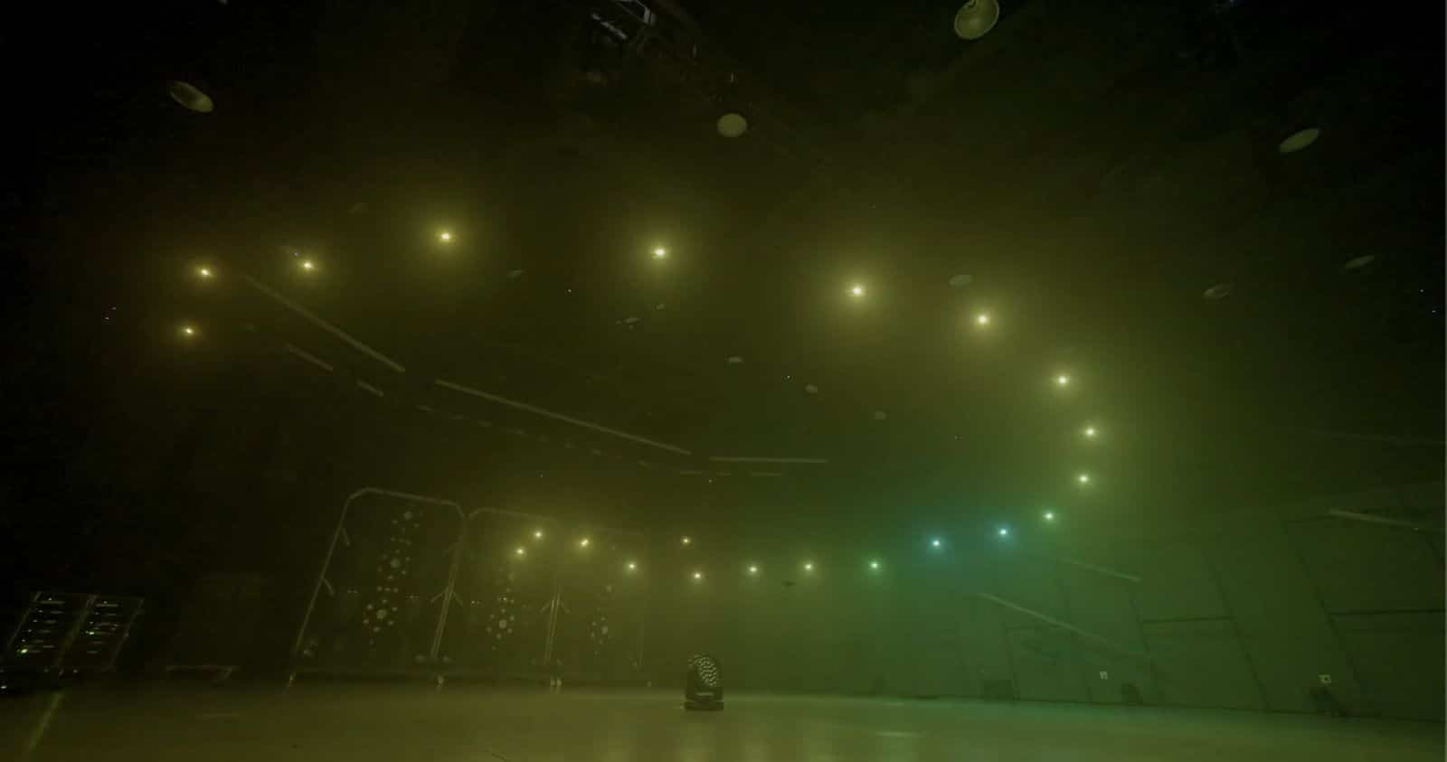 Warm drone lights curve through haze above a row of floor fixtures.