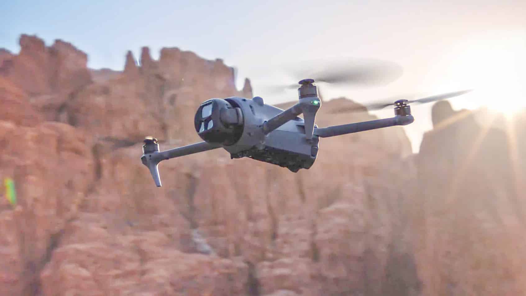 A folding camera drone banks above red rock spires in low golden light.