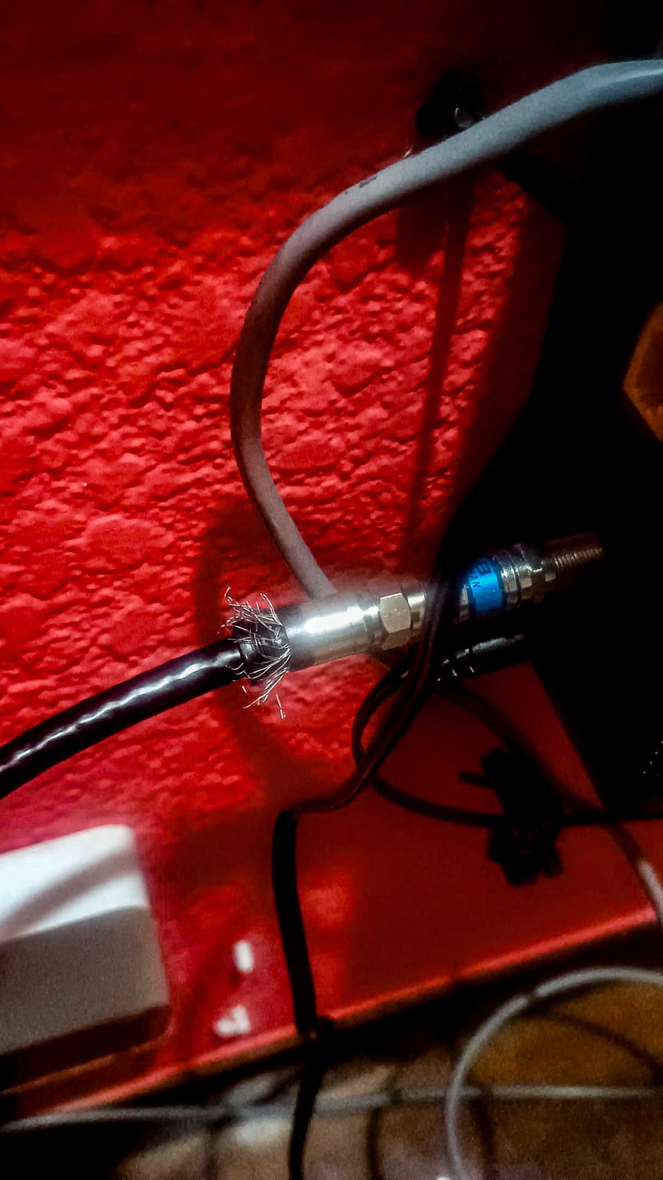 Braided shielding splays from a coaxial connector being fitted against a red wall.