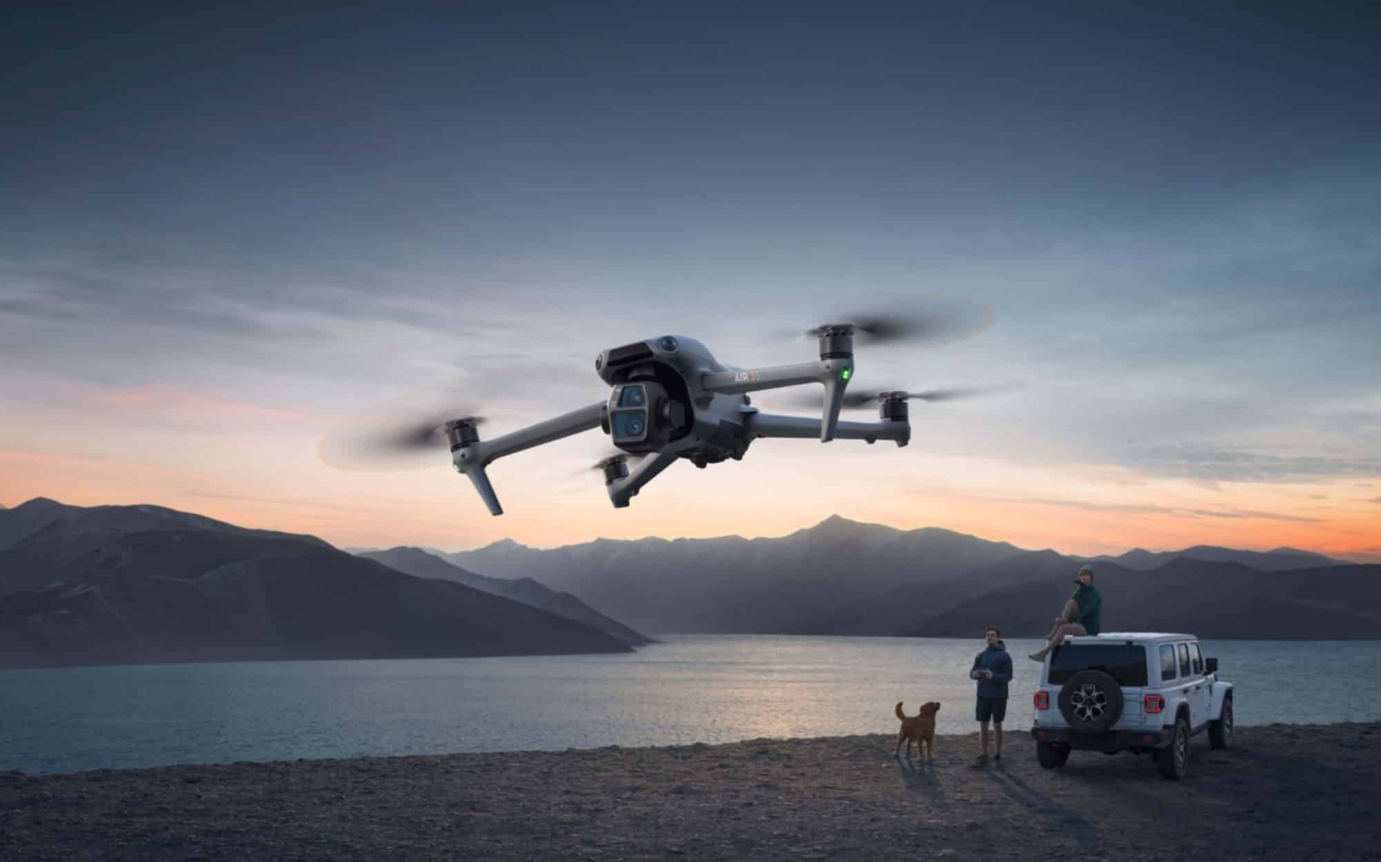 A DJI Air 3S flying at dusk over a lake as a traveler watches.