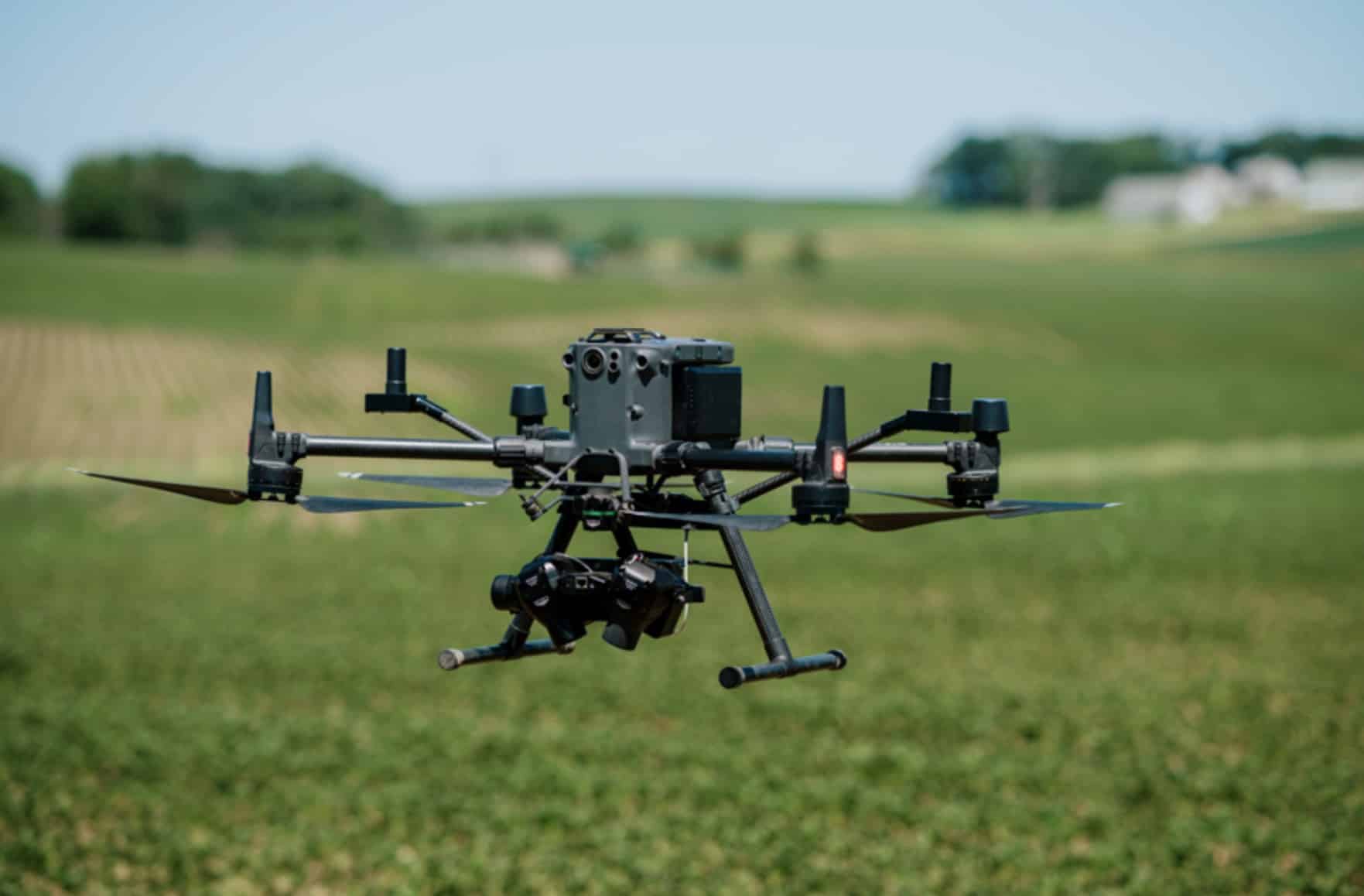 A survey quadcopter carrying a crop-imaging sensor hovers above a green field.