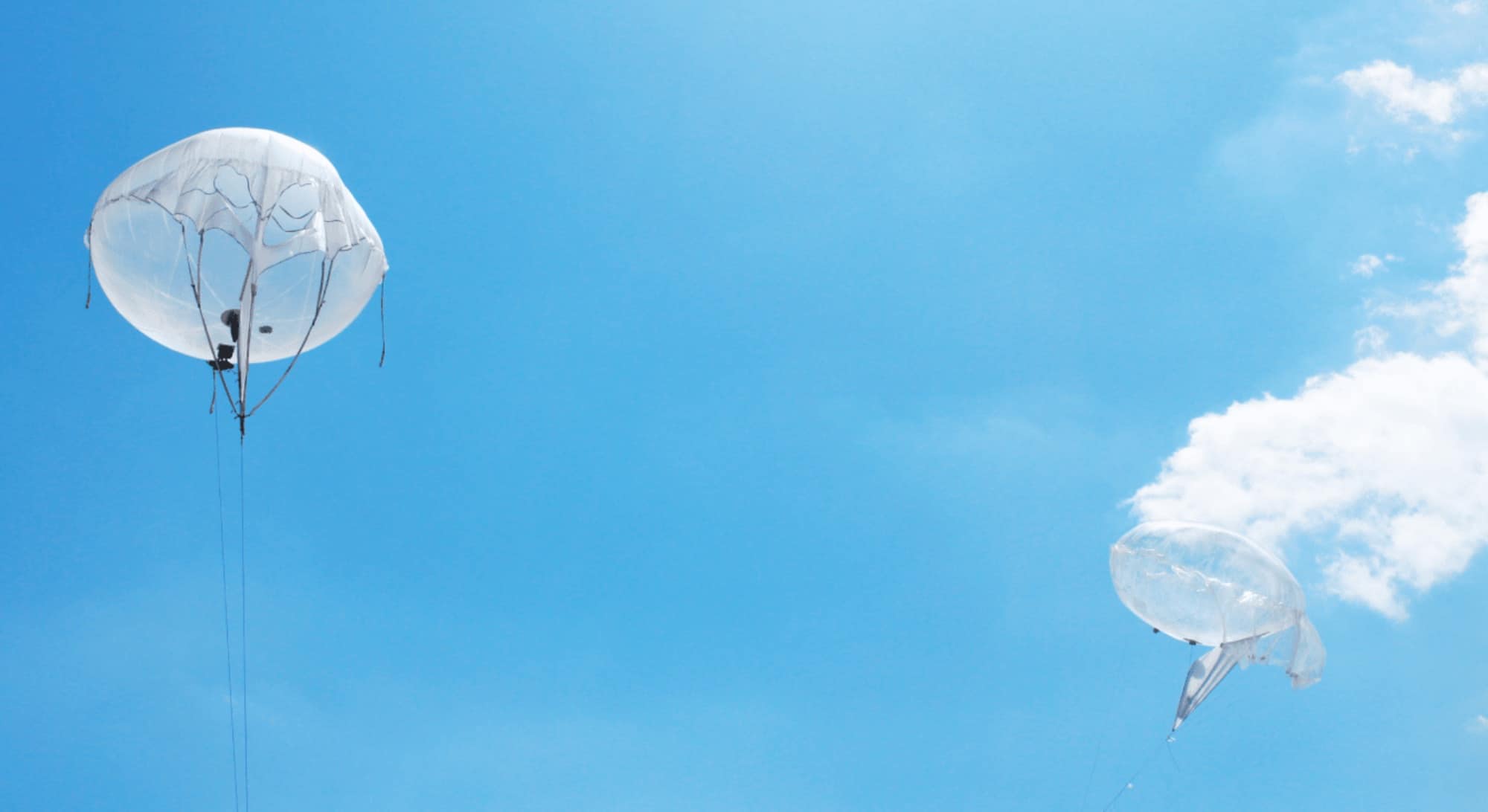 White helium balloon floats on a tether against a bright blue sky.