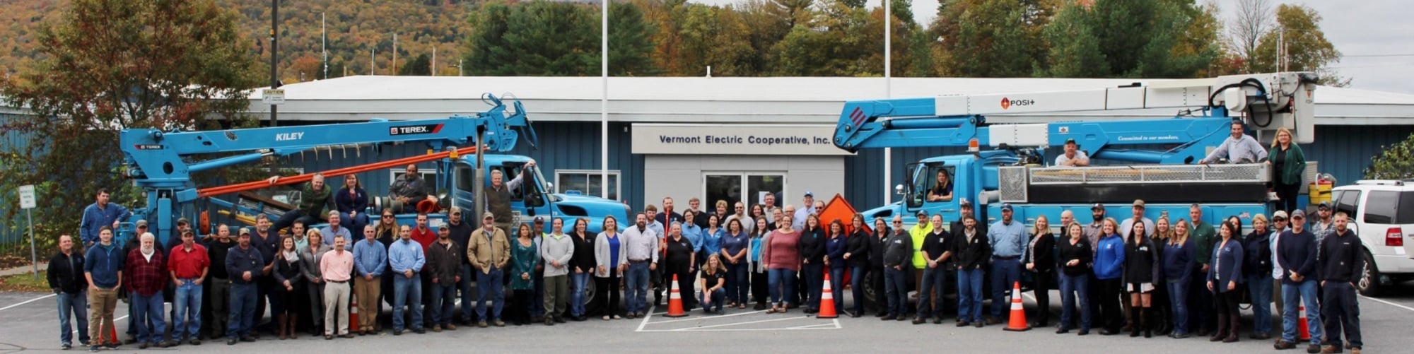 Vermont Electric Cooperative staff group photo in front of bucket trucks and headquarters.