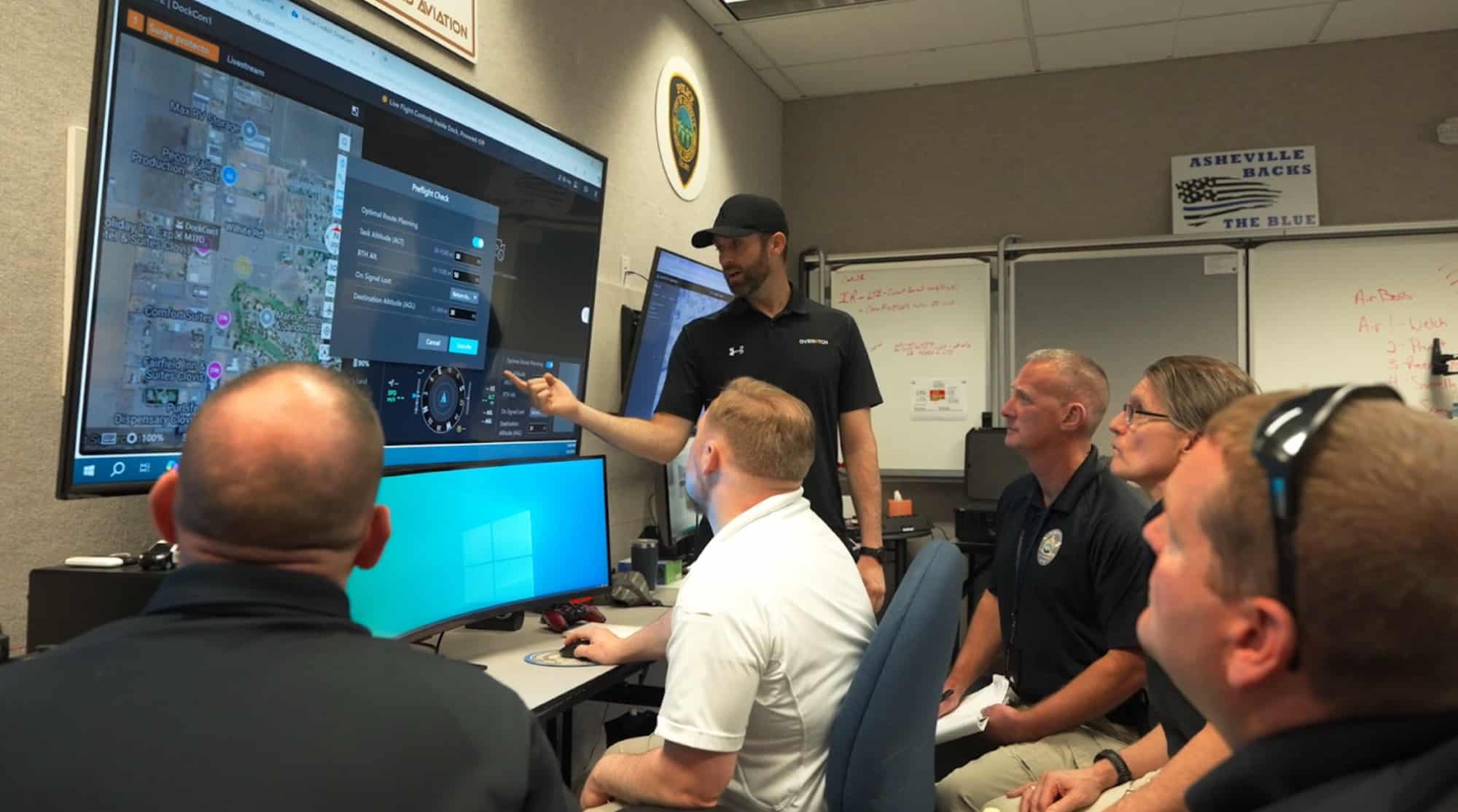Officials watching live drone feeds on monitors in an emergency operations room.