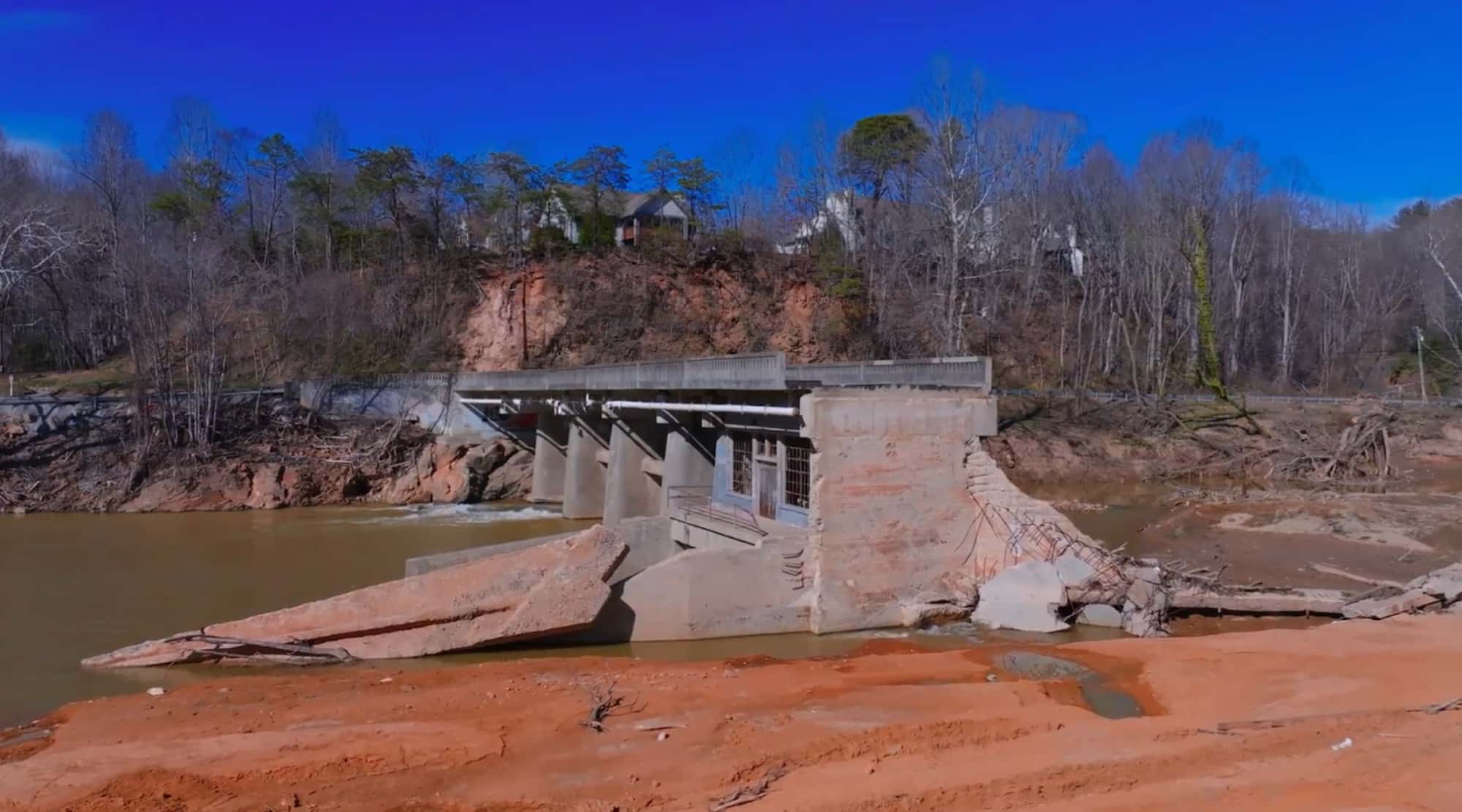 Aerial view of a collapsed concrete building beside a flood-scoured riverbank.