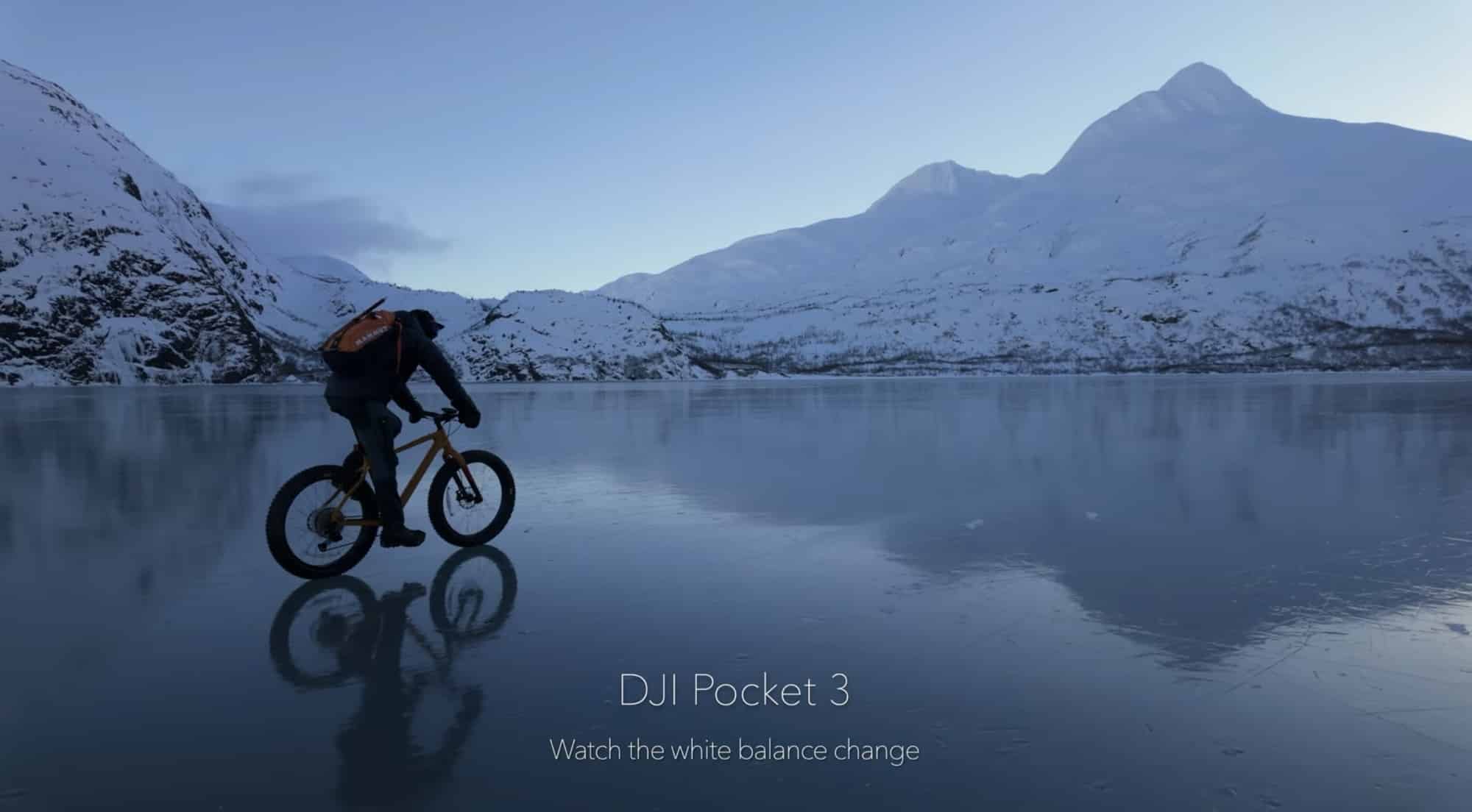 Cyclist crossing a mirror-flat lake beneath a snow-streaked peak.