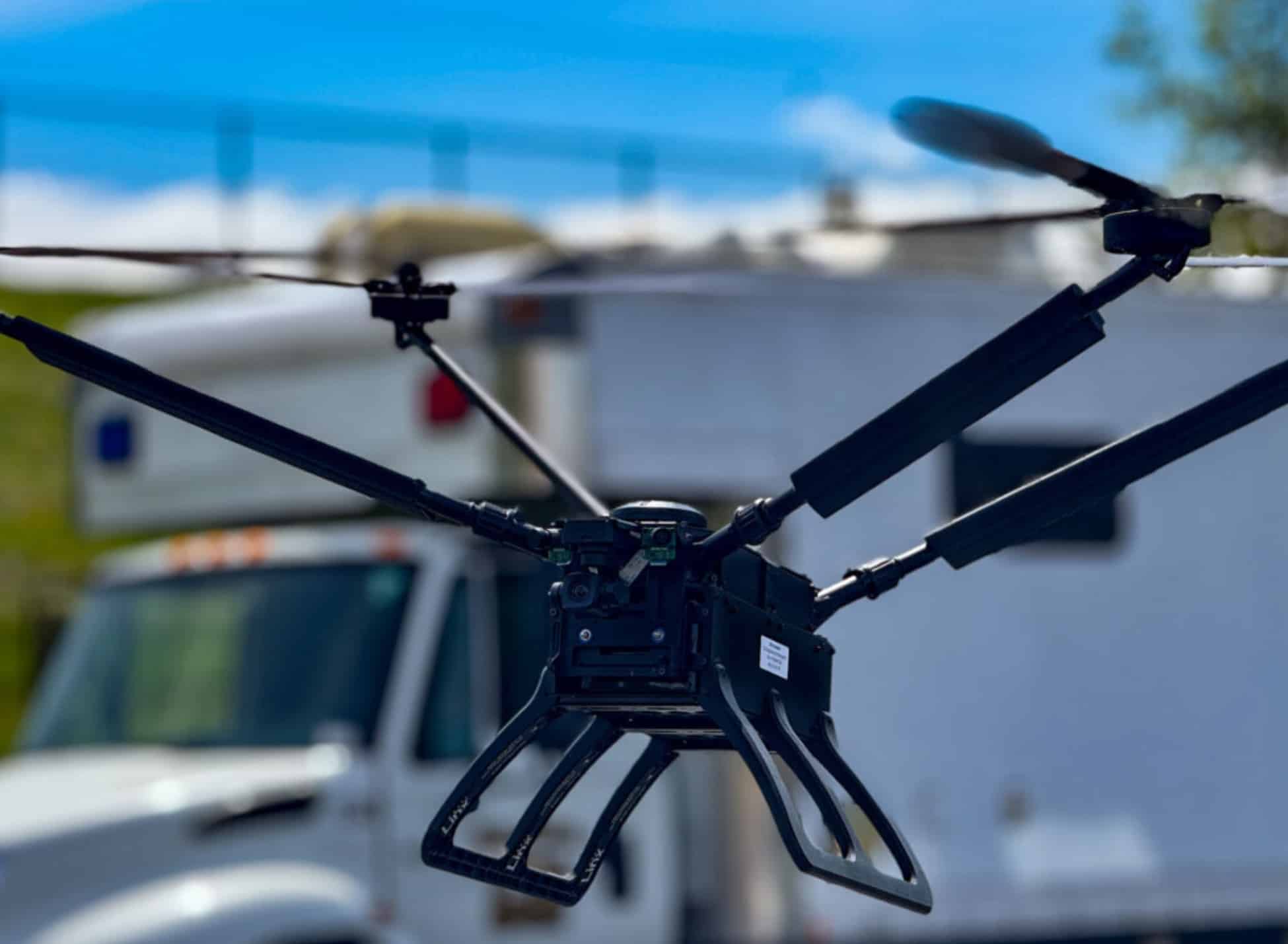 Large black quadcopter with skid landing gear parked beside a white response truck.