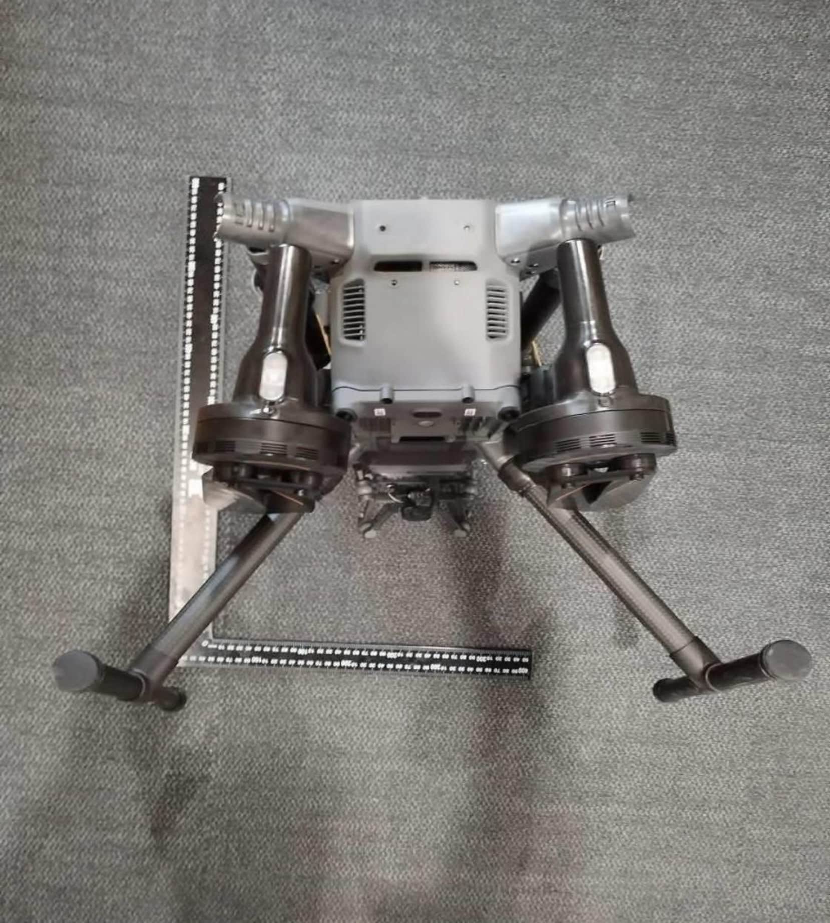 The drone stands on tall landing legs, viewed from behind on the lab mat.