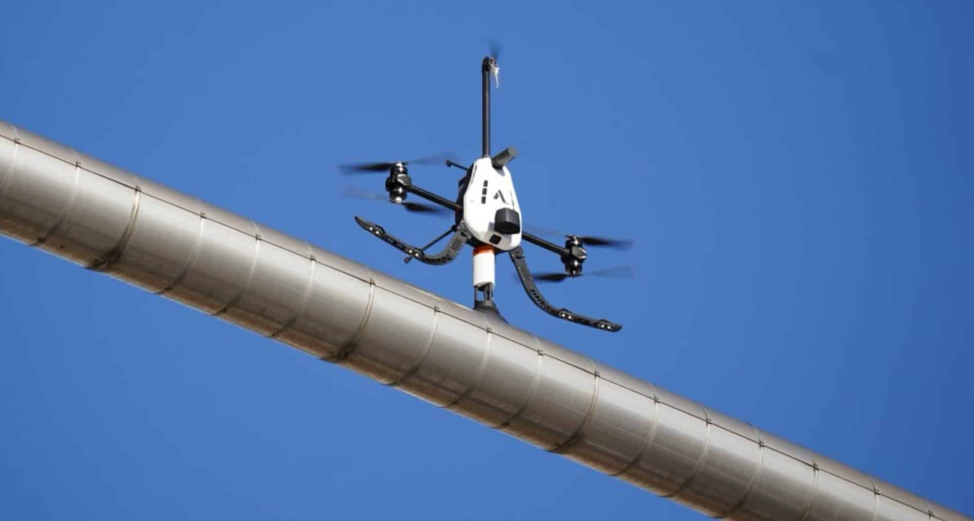 A tilting-rotor inspection drone presses its sensor against an elevated metal pipe.