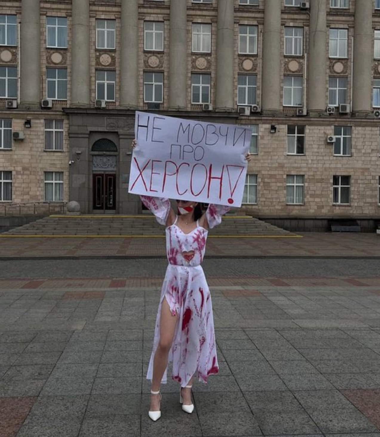 Protester in a blood-stained white dress holding a placard about Kherson.