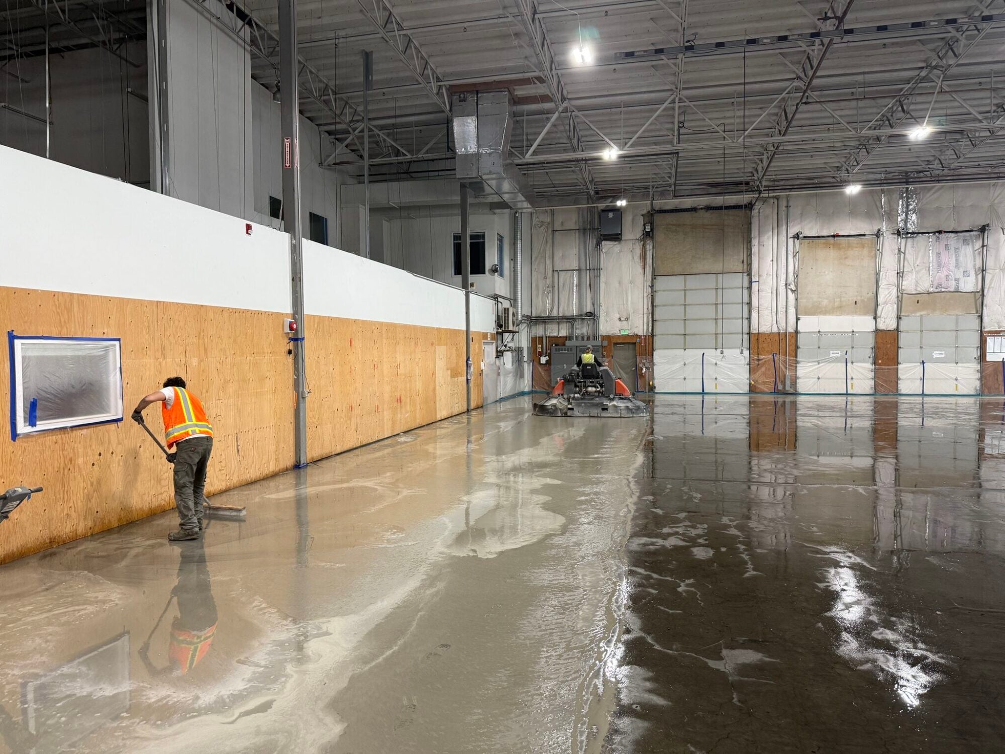Worker in a hi-vis vest polishing the wet concrete floor of the warehouse.