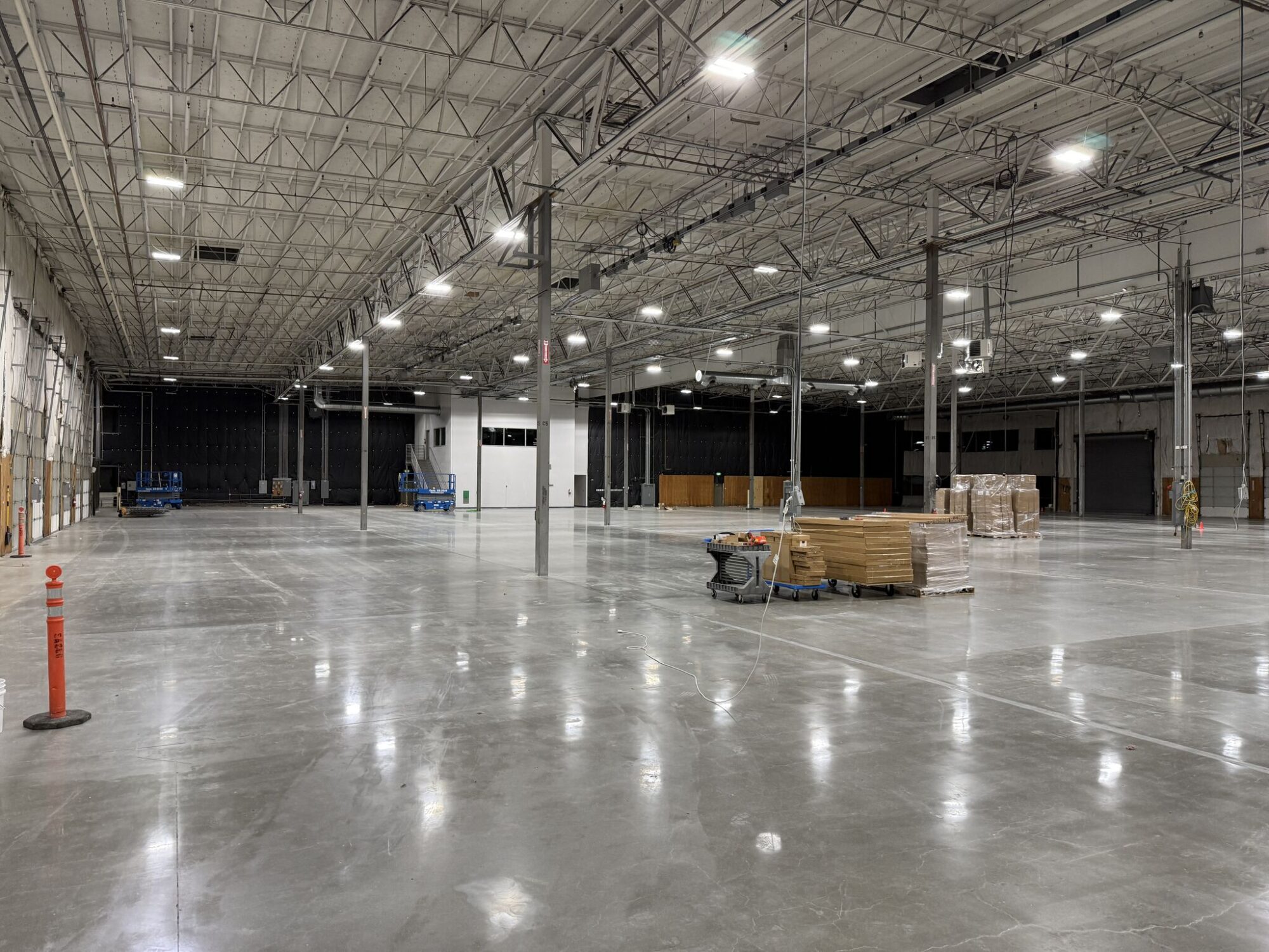 Wide empty warehouse bay with polished floor, pallets and overhead lighting.