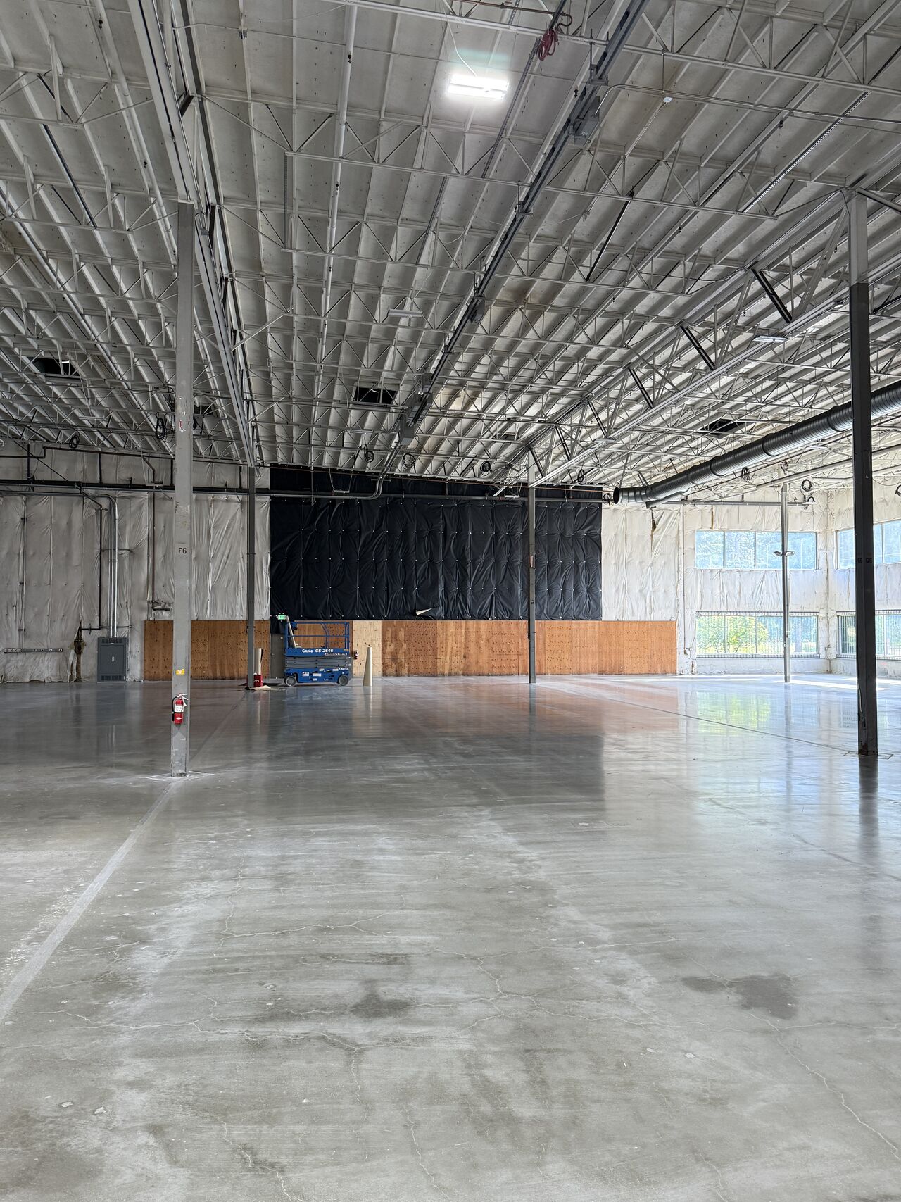 Warehouse interior with a black curtain wall and a lone floor machine.
