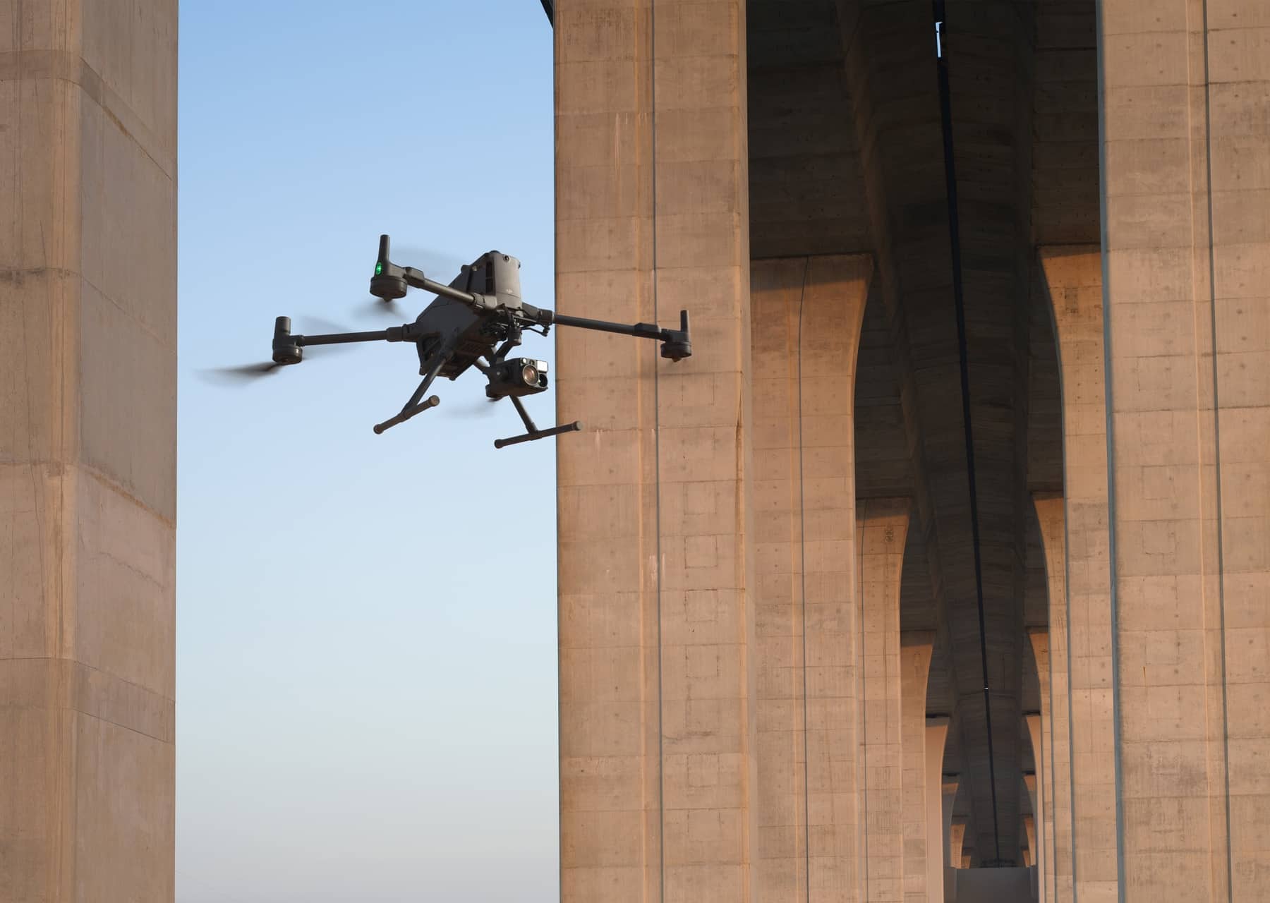 Matrice 400 flies between the massive concrete piers of a bridge.