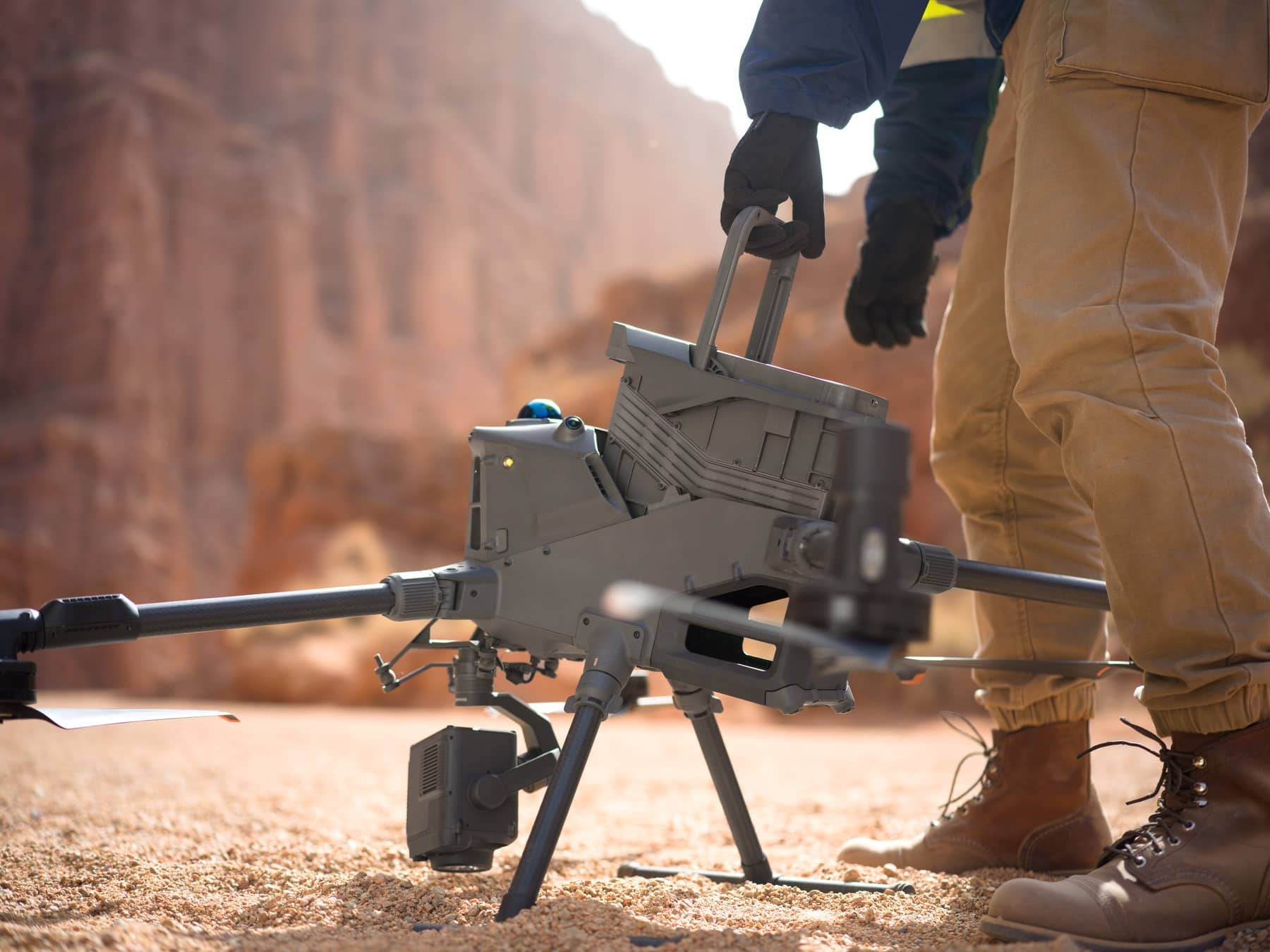 Gloved operator lifts the DJI Matrice 400 by its handle on desert ground.