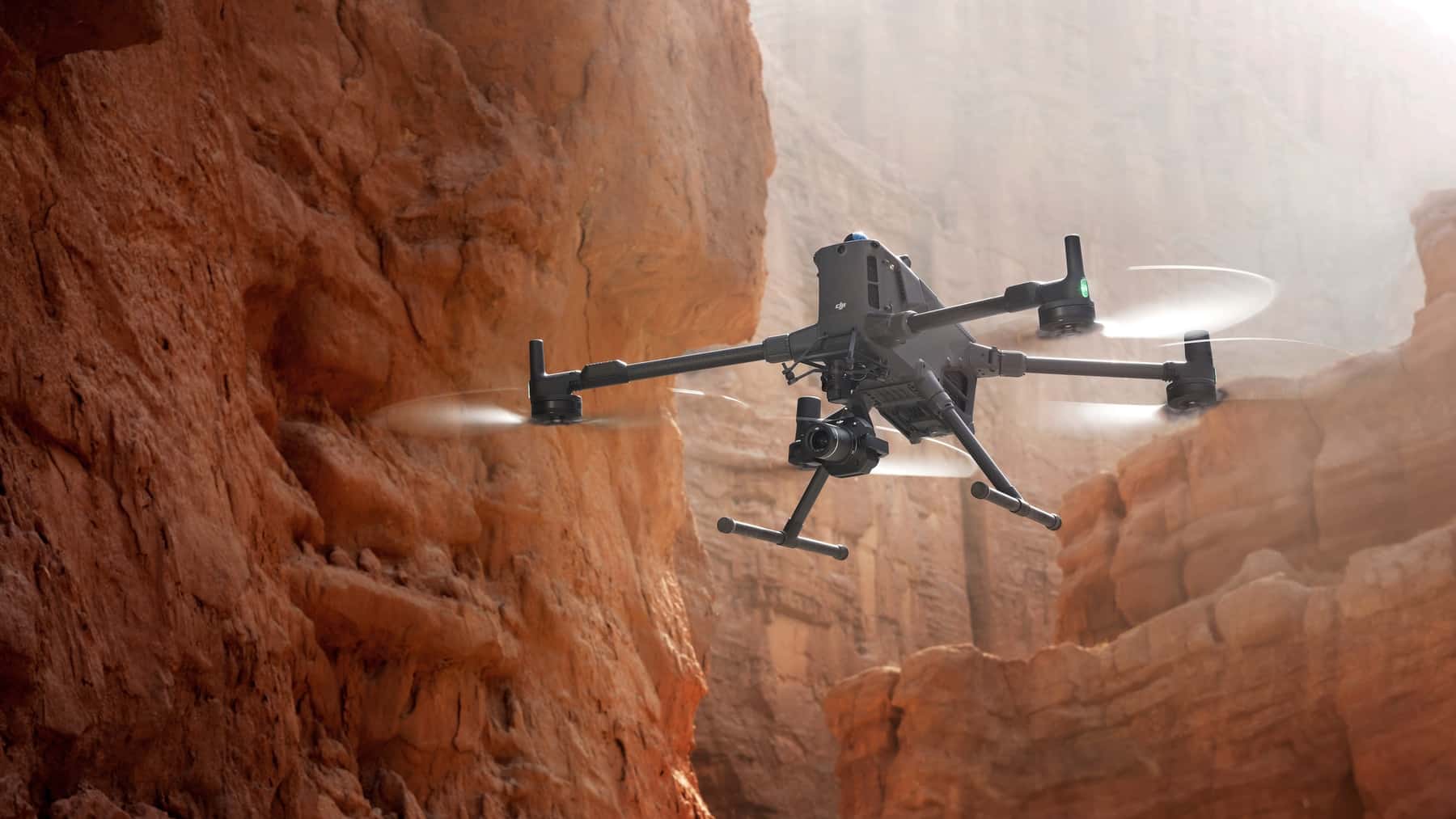 The quadcopter skims close to a layered red sandstone cliff face.