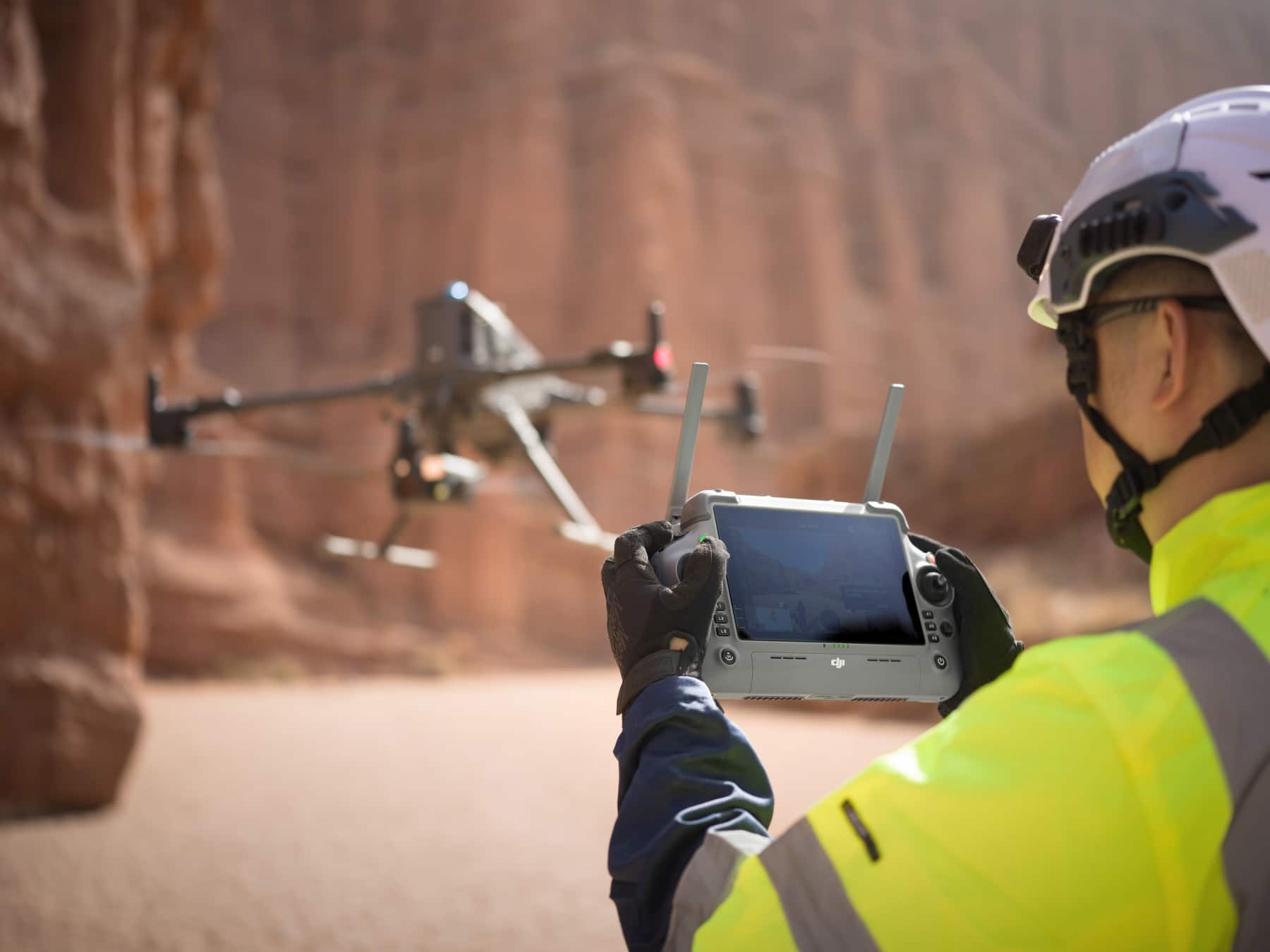 Pilot in a white helmet flies the Matrice 400 using a touchscreen controller.