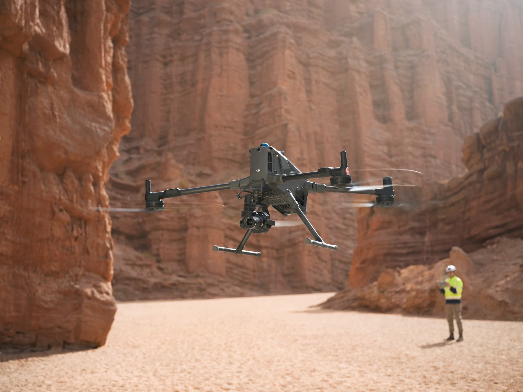 Rotor wash kicks up dust as a lone operator watches from the canyon floor.
