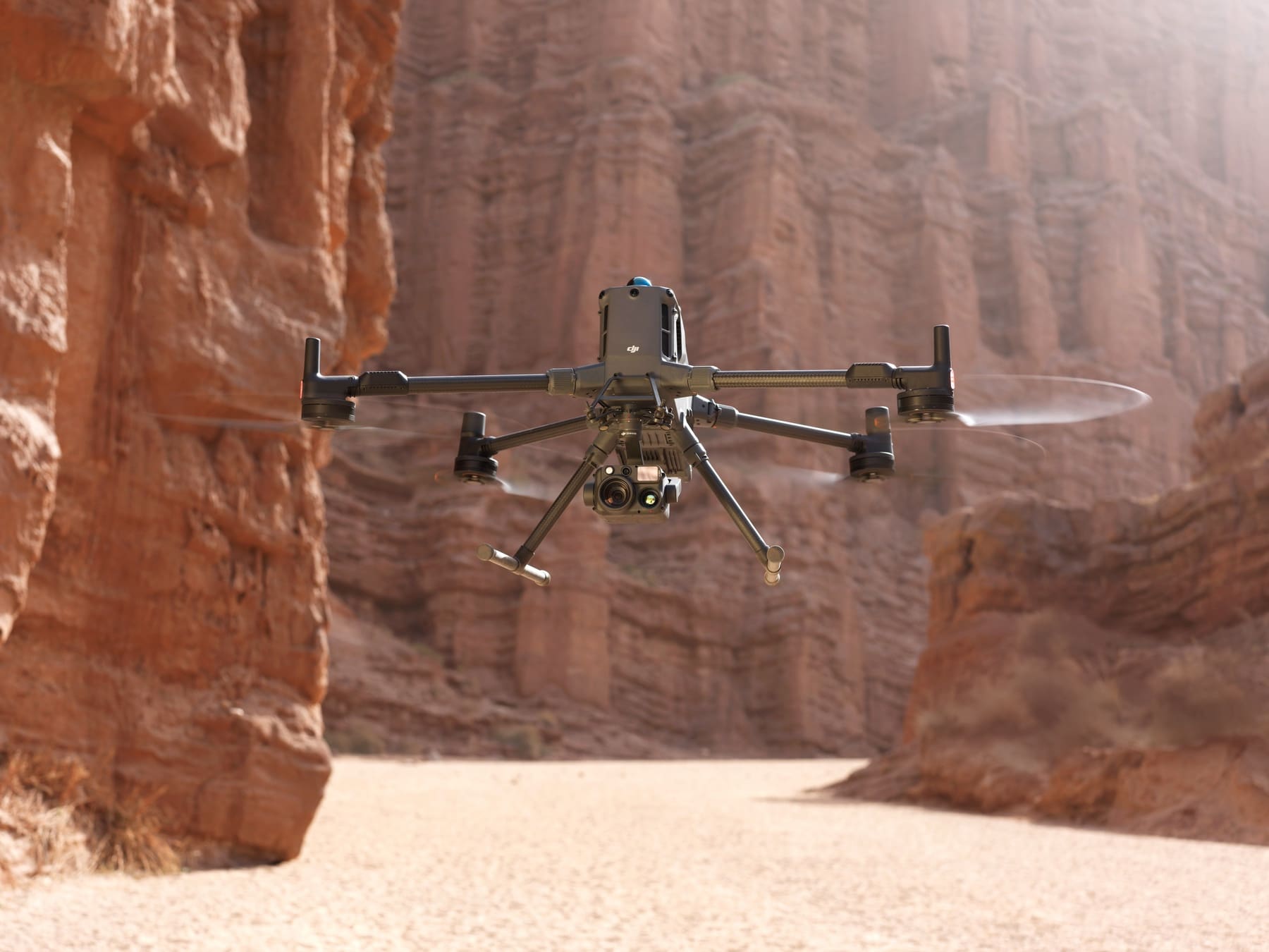 Matrice 400 hovers beside a towering red rock wall with gimbal payload attached.