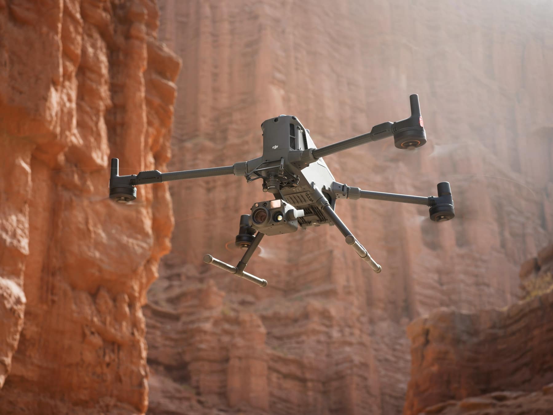 The drone banks over sand while flying through an eroded canyon.