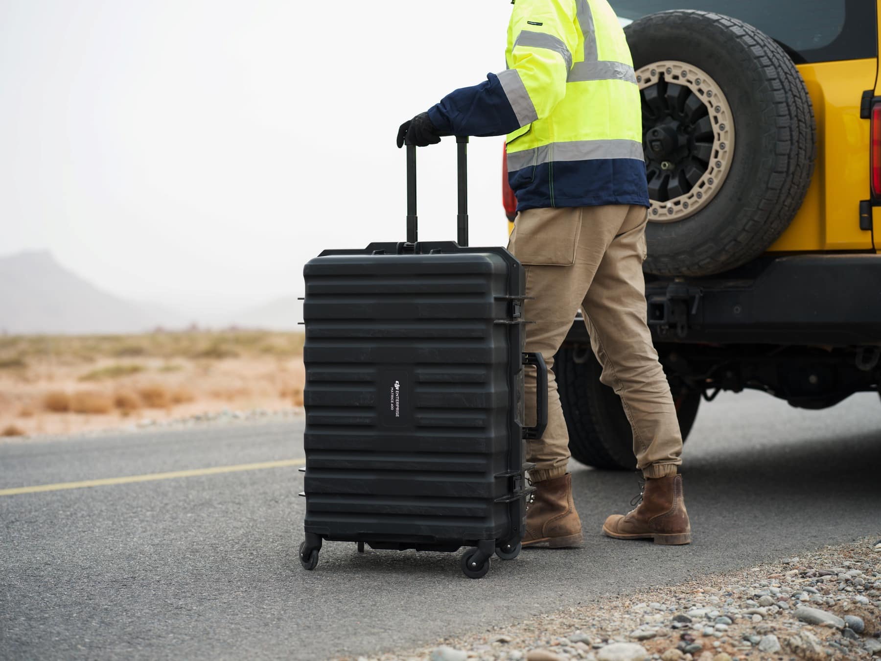 The rolling transport case is pulled past the rear wheel of a yellow truck.