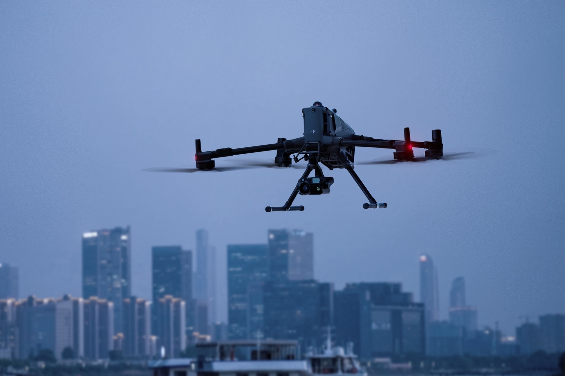Matrice 400 hovers at blue hour above a river with high-rise towers behind.
