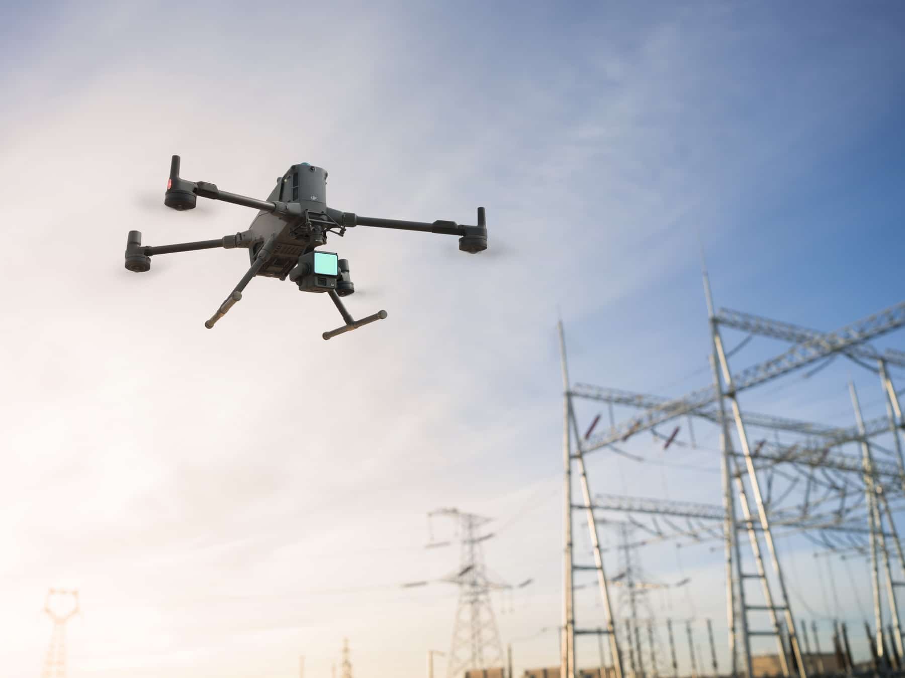 The drone flies past a cluster of high-voltage transmission towers and wires.