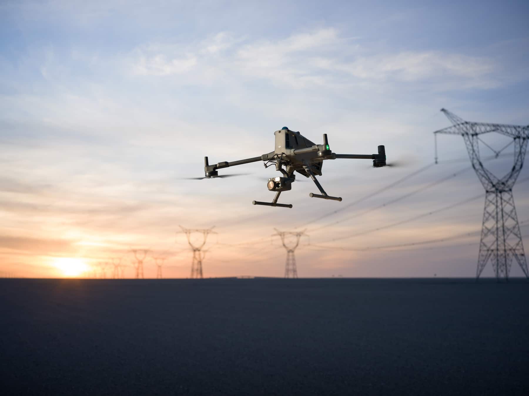 Silhouetted against a sunset, the drone inspects a line of electricity pylons.