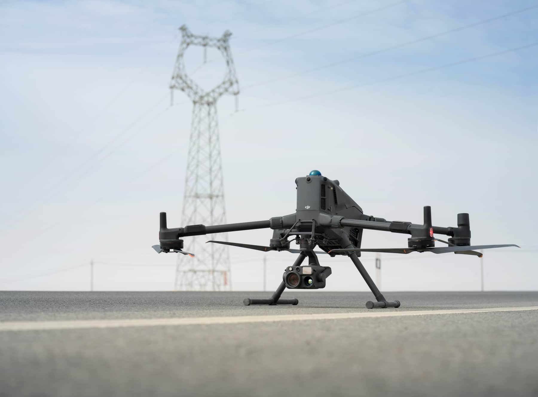 Matrice 400 rests on pavement in front of a lattice transmission tower.