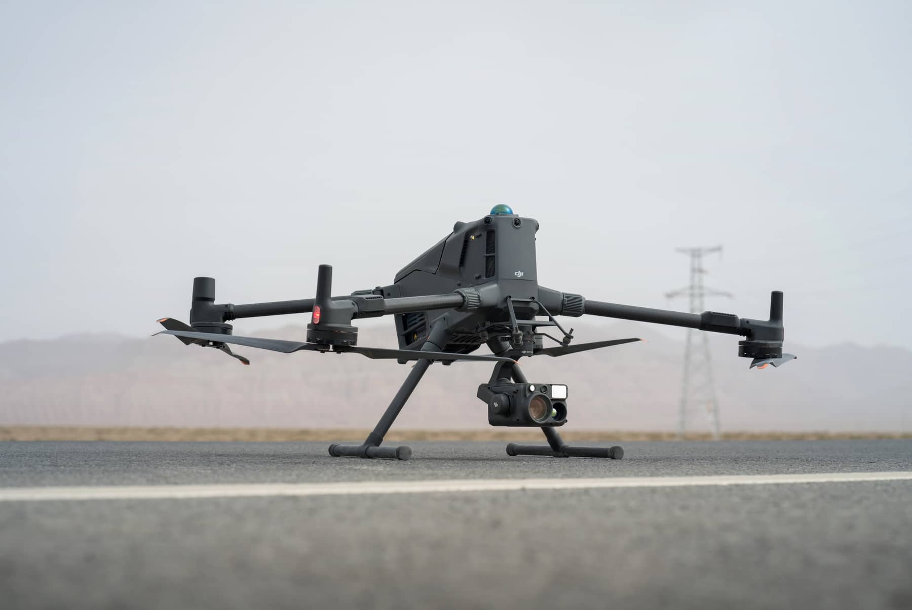 The unfolded drone sits on a road with a power pylon in hazy distance.