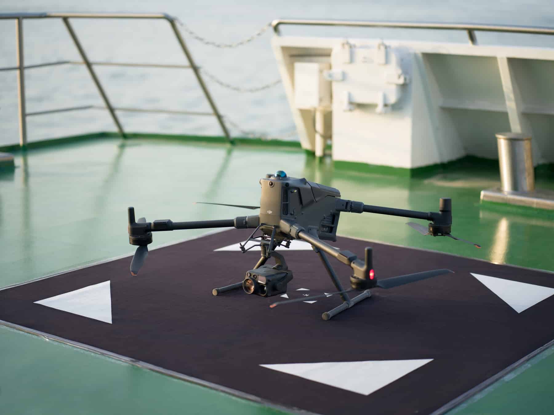 Landing pad marked with white arrows holds the drone on a green ship deck.