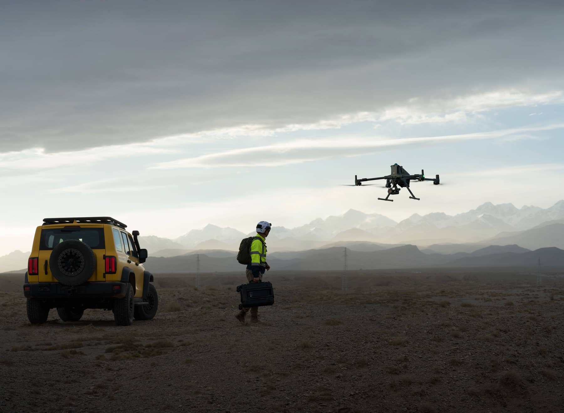 Crew member carries a case toward a yellow truck as the drone climbs away.