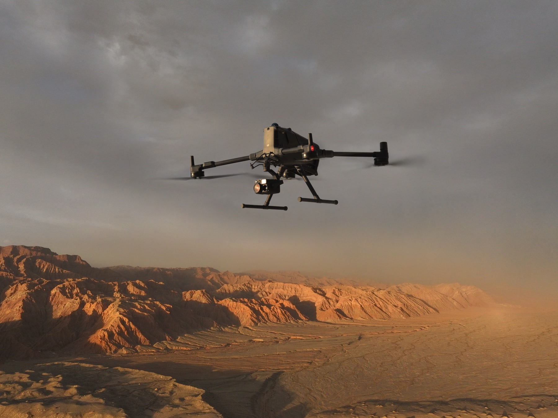 Drone flies over red badlands under heavy dust-filled cloud at golden hour.