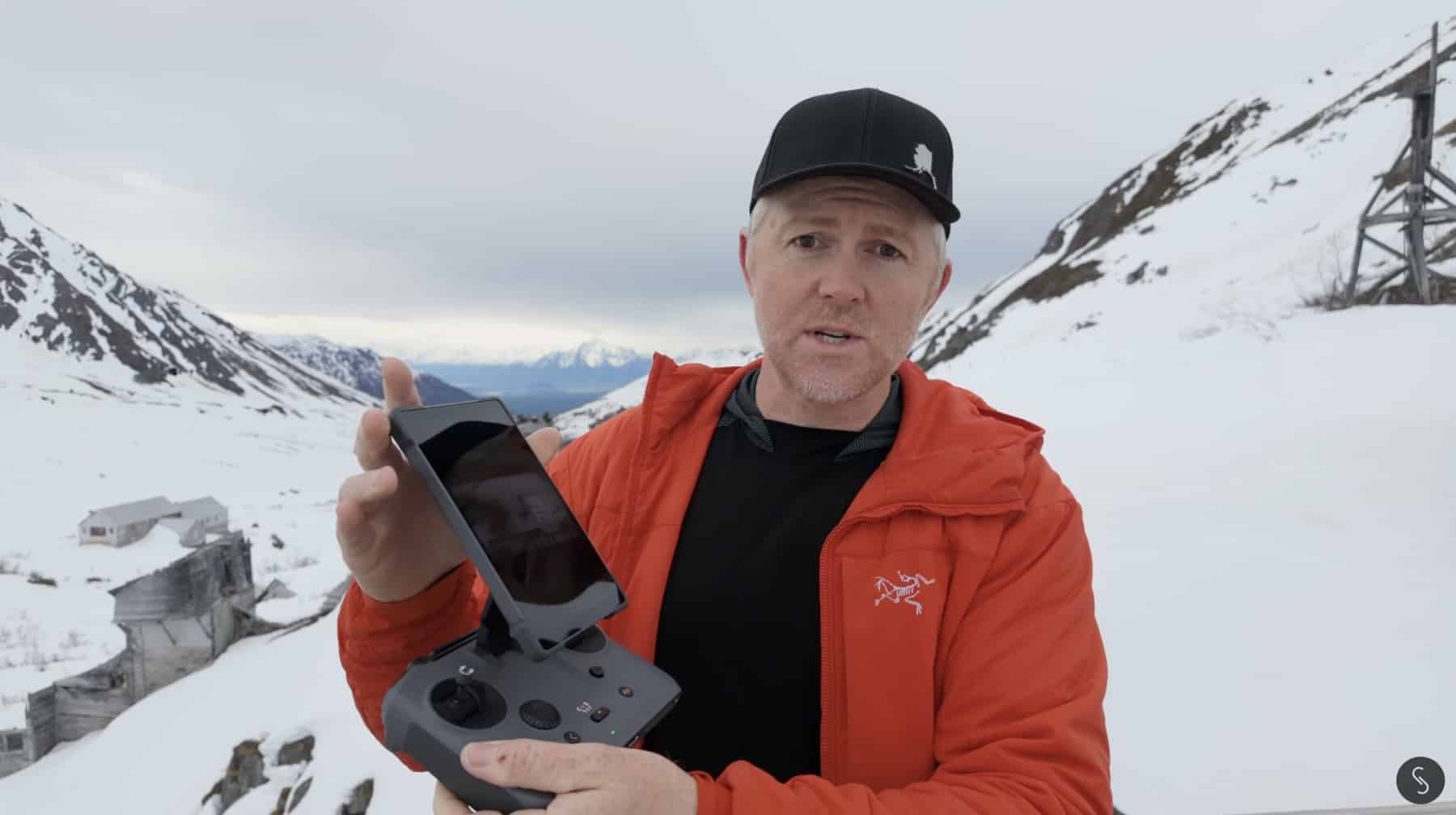 A reviewer in a red jacket holds a screen controller on a snowy hillside.