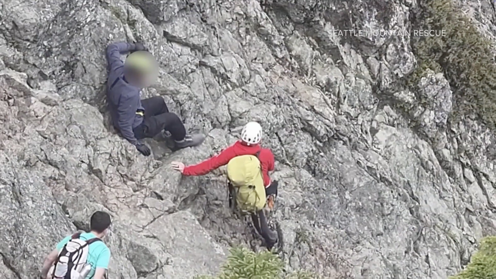 Drone frame of Seattle Mountain Rescue crews reaching an injured hiker on a rocky slope.