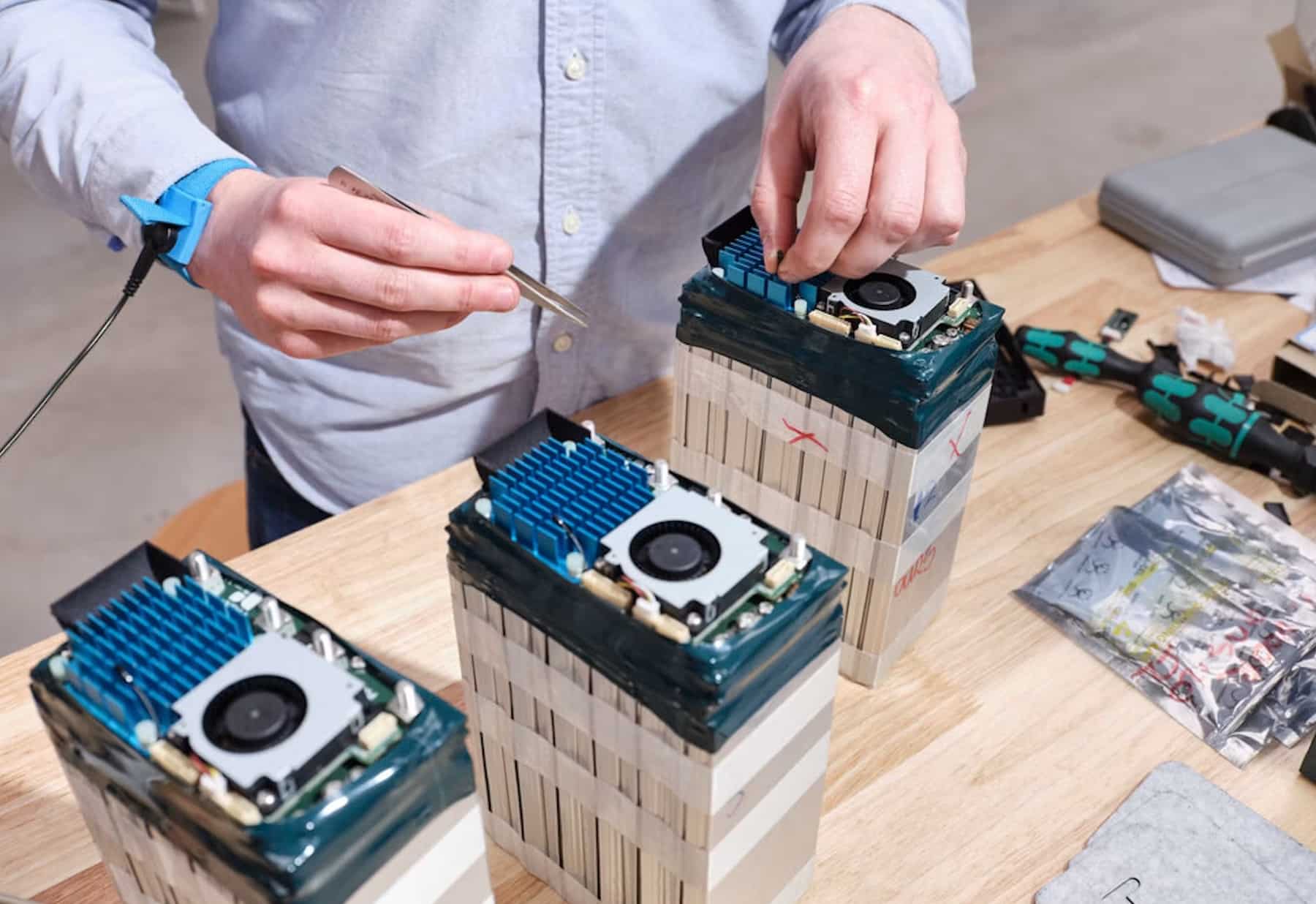 Technician assembles stacked custom drone battery packs with cooling fans on a workbench.