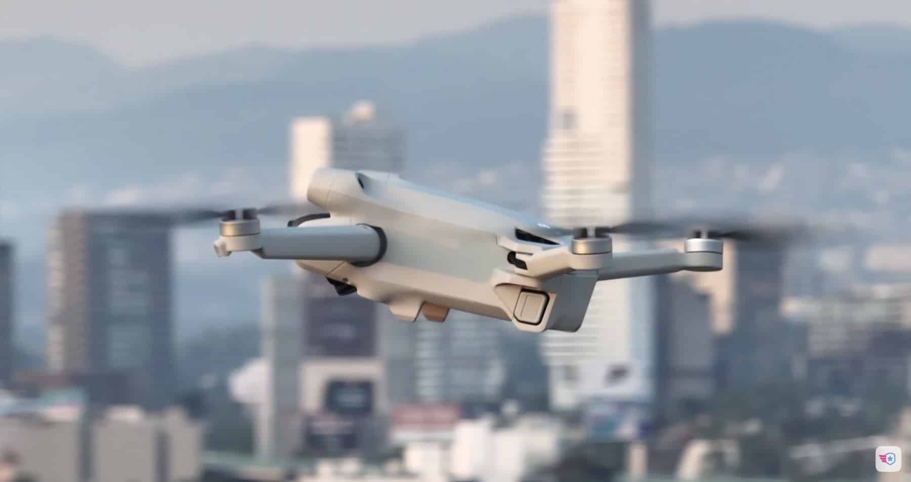 A small folding drone hovers above a hazy city skyline backed by mountains.