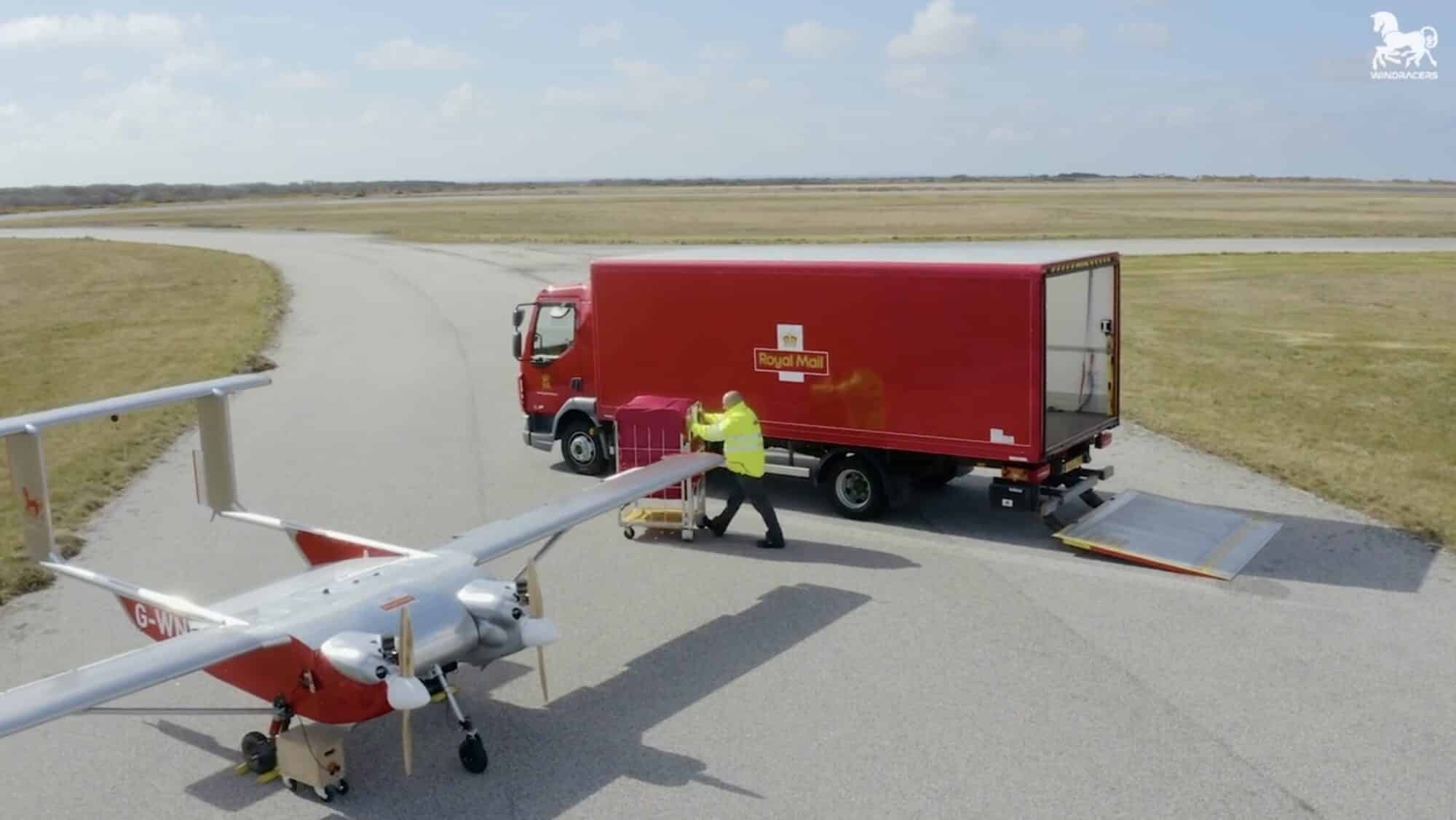Fixed-wing cargo drone on a runway as crew loads a red delivery truck.