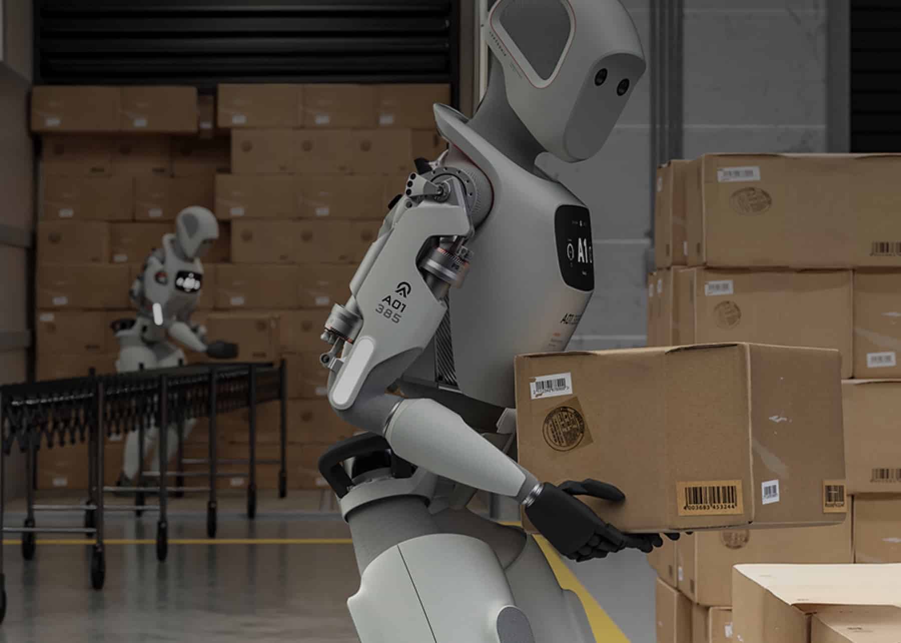 Humanoid robots move cardboard boxes onto a conveyor inside a warehouse.