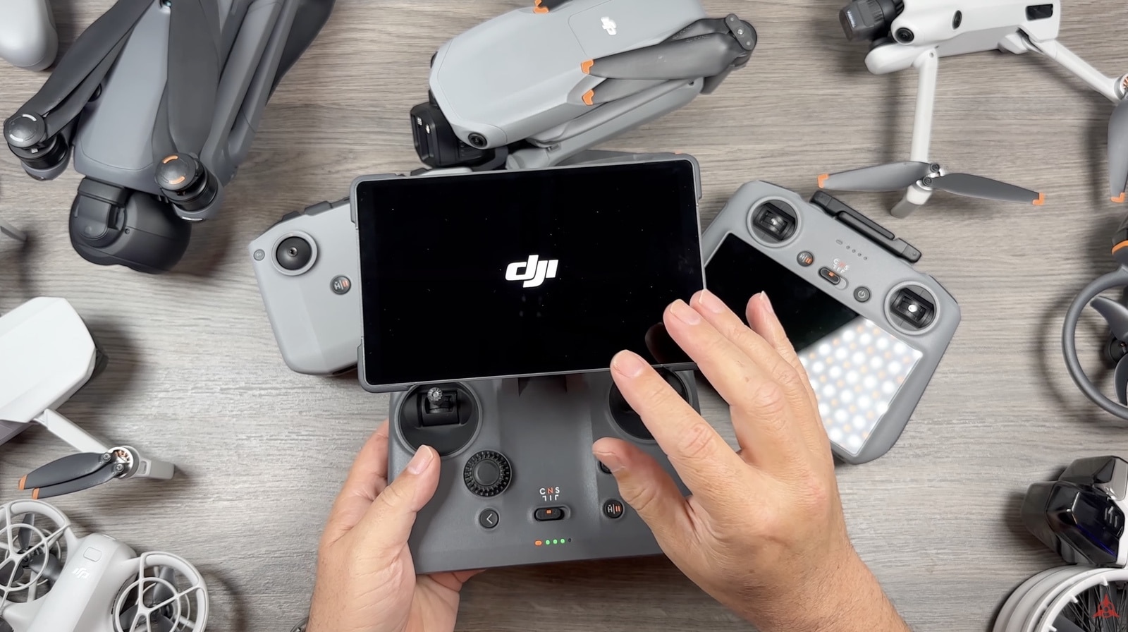 Hands hold a screen-equipped controller booting to the DJI logo on a cluttered desk.