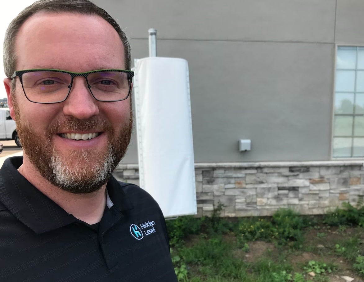 A company employee smiles beside a white airspace sensor mounted on a building.