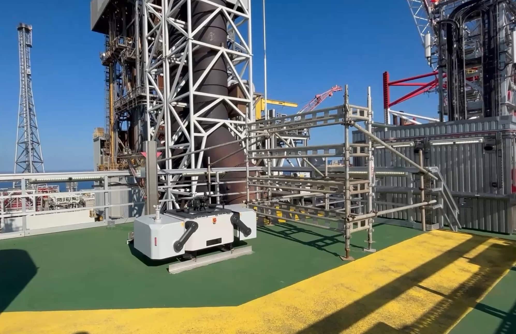 A white drone docking station installed on the green deck of an offshore platform.